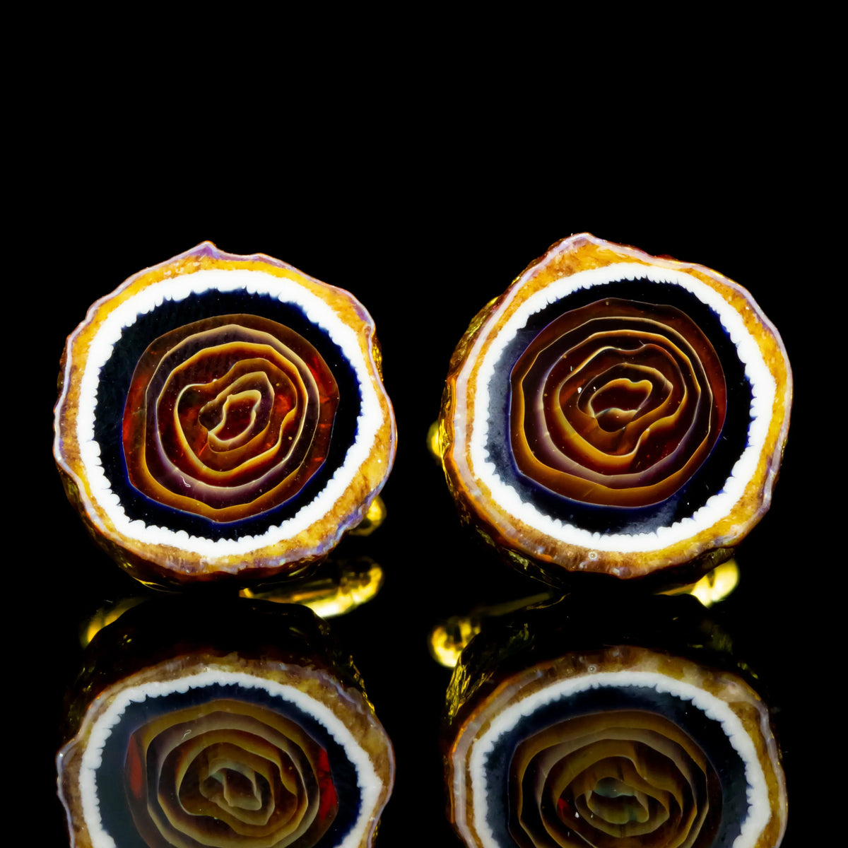 Golden agate stone cufflinks with polished concentric rings on a glossy black surface