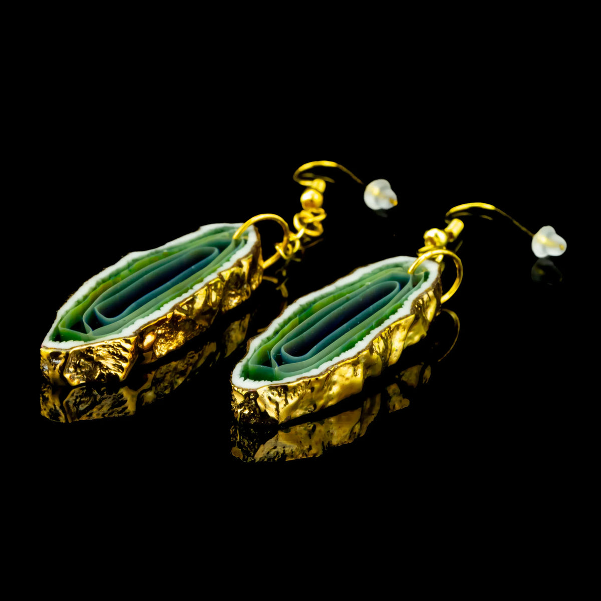 Green agate elongated earrings with gold trim, displayed on black reflective surface