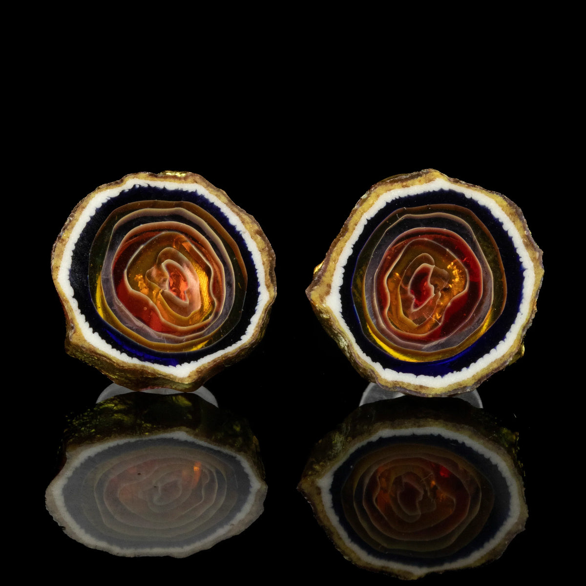 Golden agate stud earrings with concentric bands, displayed on black reflective surface
