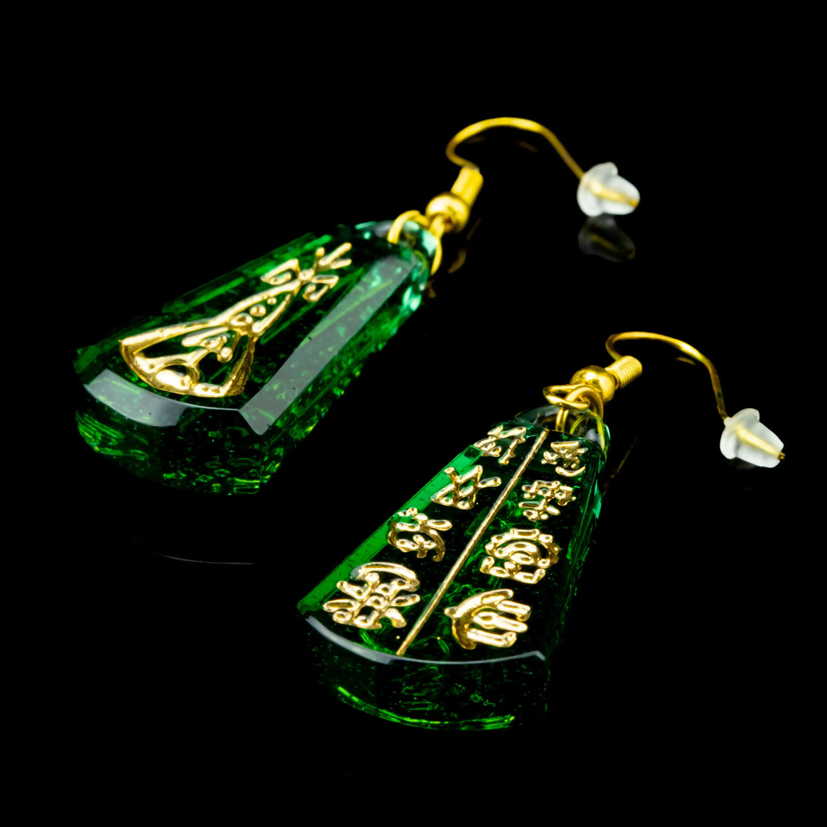 Green glass dangle earrings with gold accents and engraved geometric designs on black background