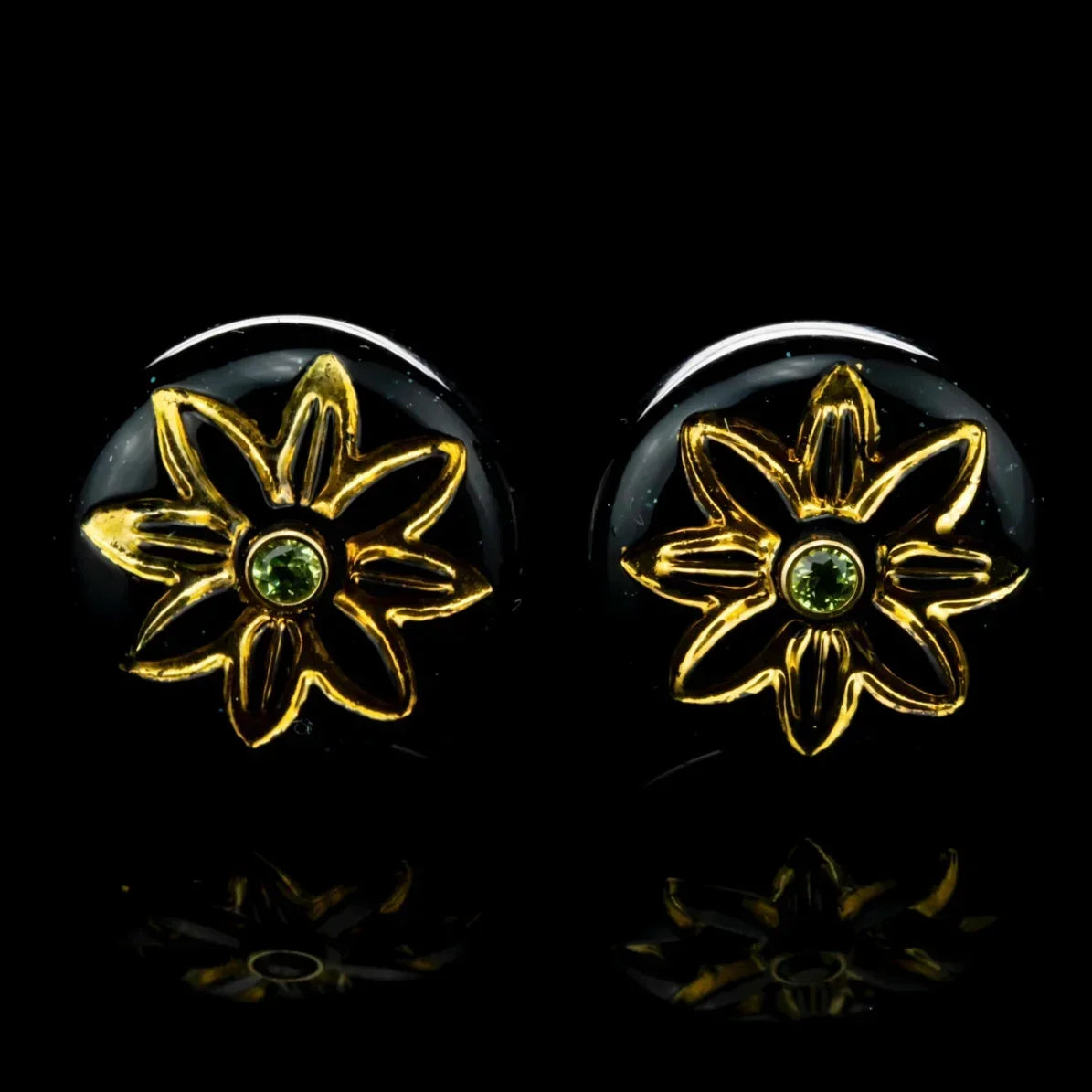 Gold flower stud earrings with green peridot gemstone centers on a black background