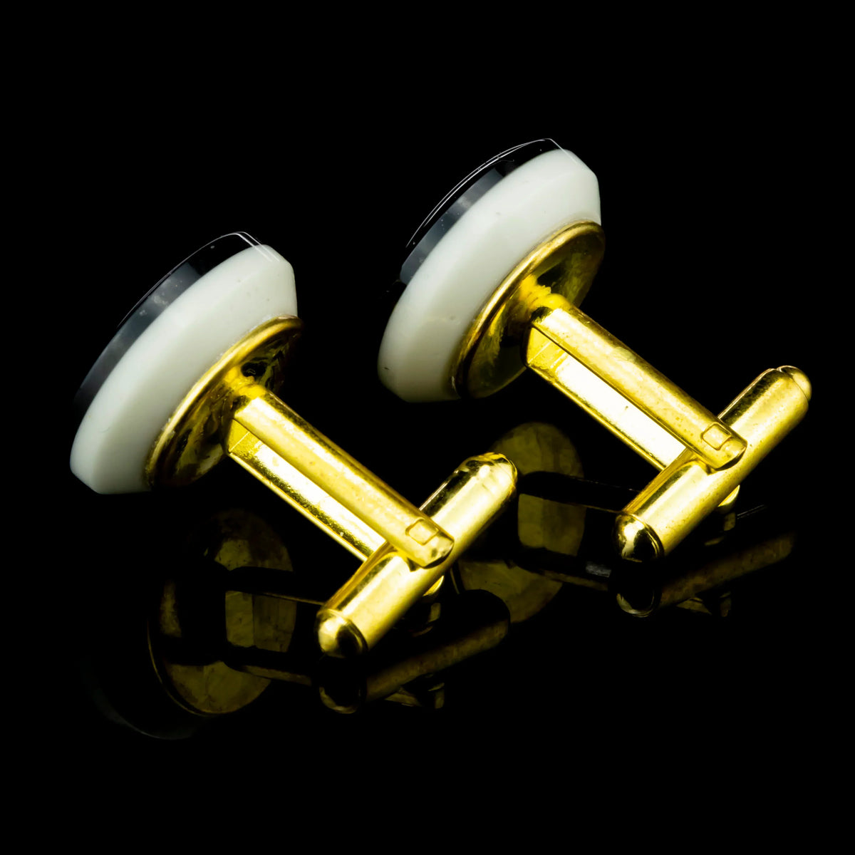 Gold and white round cufflinks with reflective black background, elegant accessory