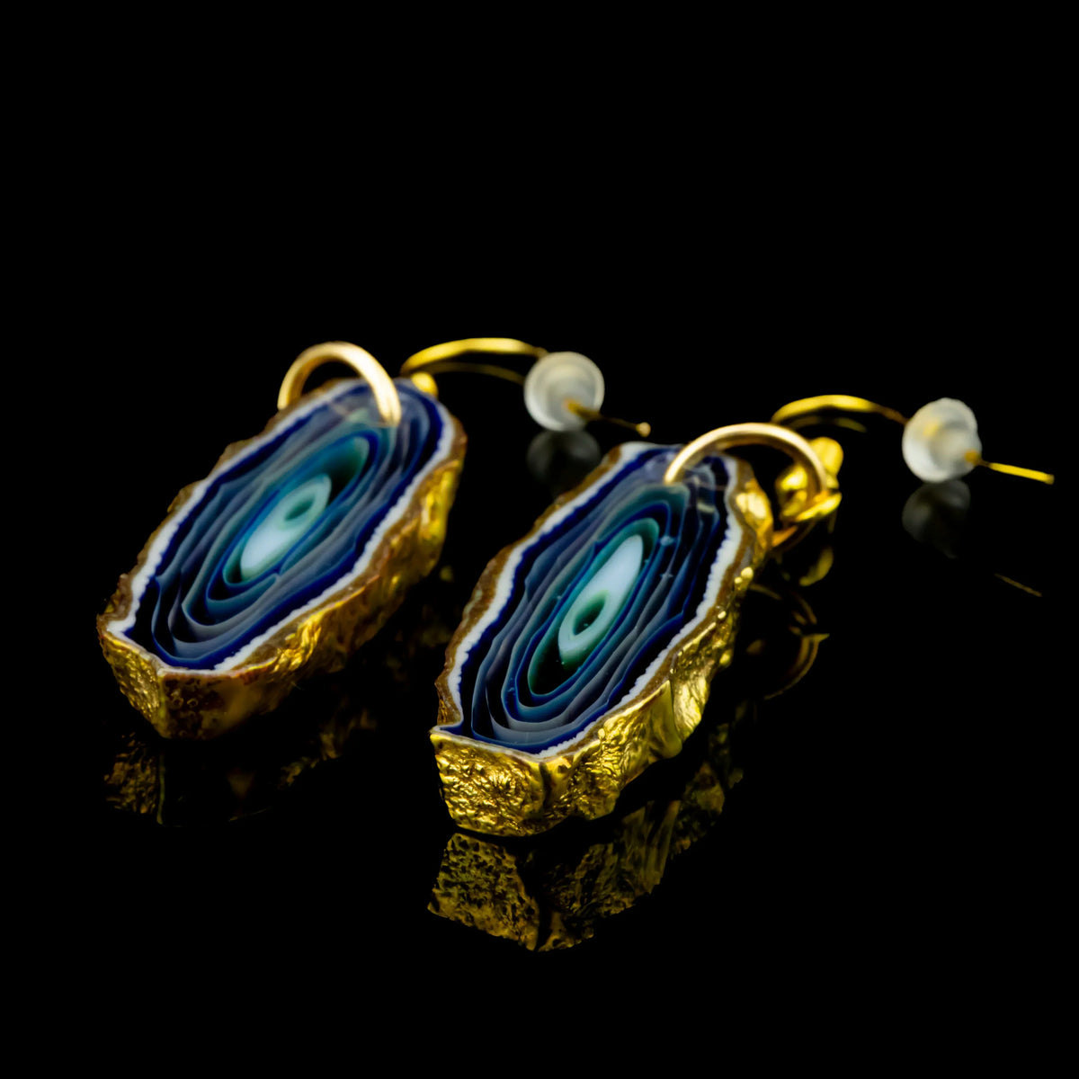 Blue and gold agate slice earrings with layered patterns on a black background