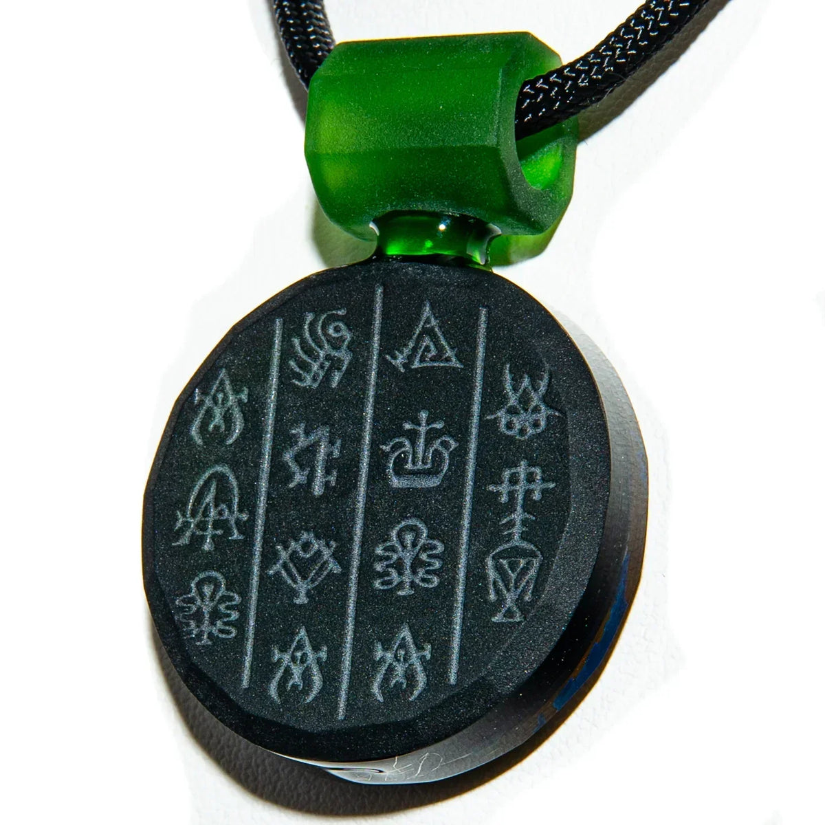 Black and green glass pendant necklace with engraved abstract symbols and braided cord.