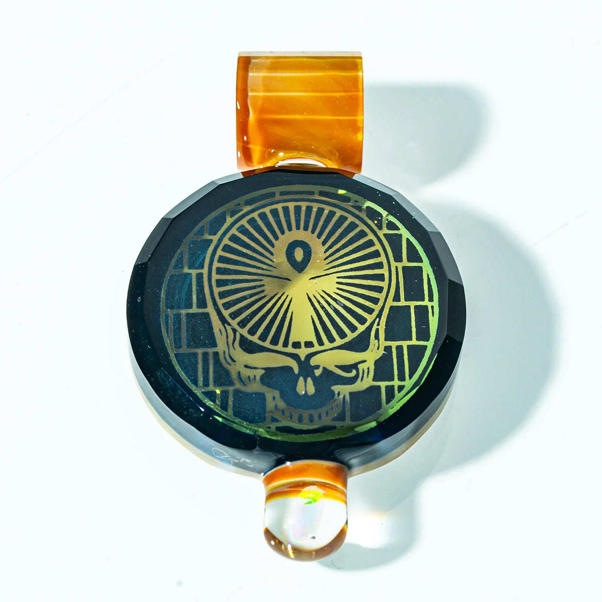 Glass pendant with gold skull design and orange loop, heady glass accessory on white background