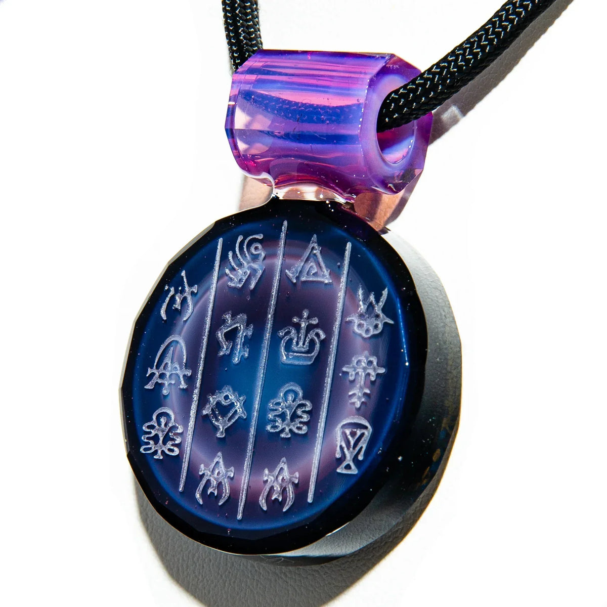 Purple and green glass pendant with engraved symbols on a black cord necklace