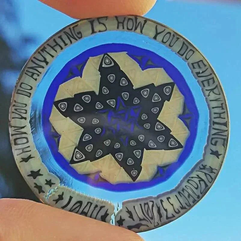 Glass coin with star mandala design, geometric patterns, and engraved quote on the rim