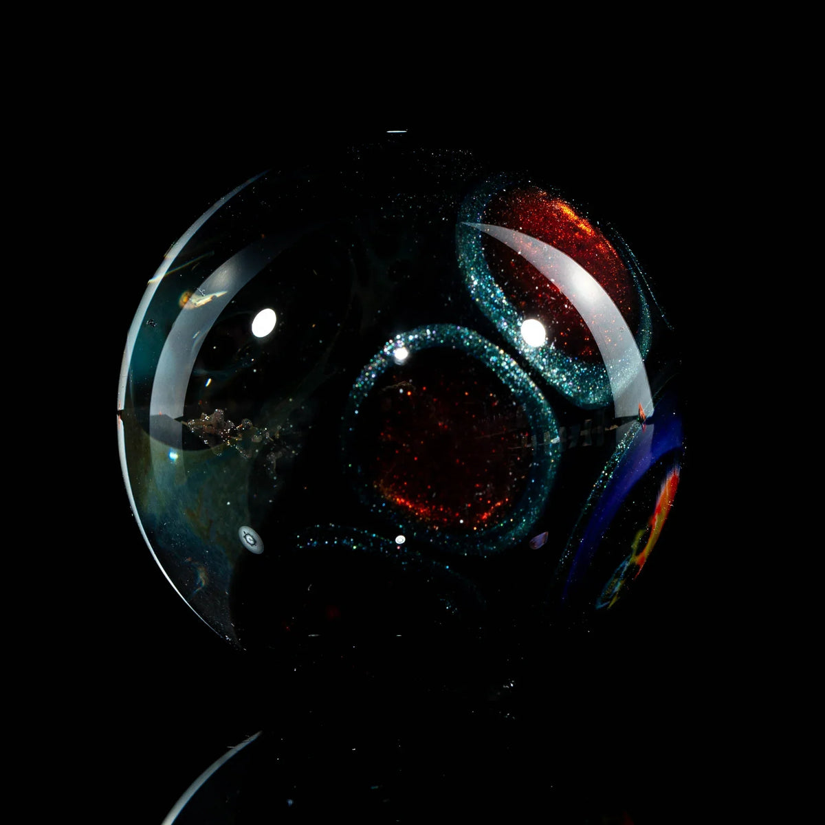 Hand-blown glass marble with shimmering red and blue circular patterns on a black background