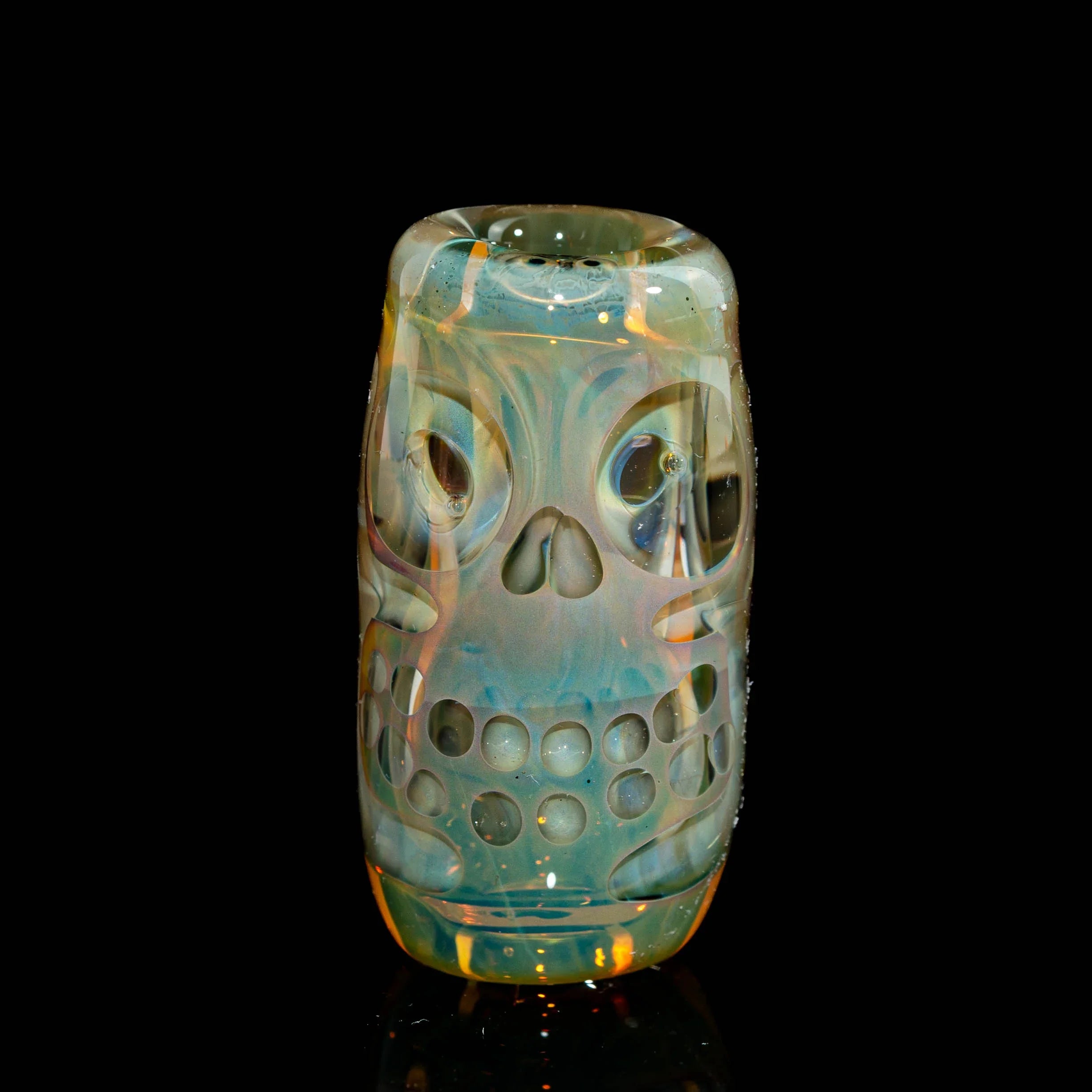 Iridescent glass pipe shaped like a skull with intricate details on a black background
