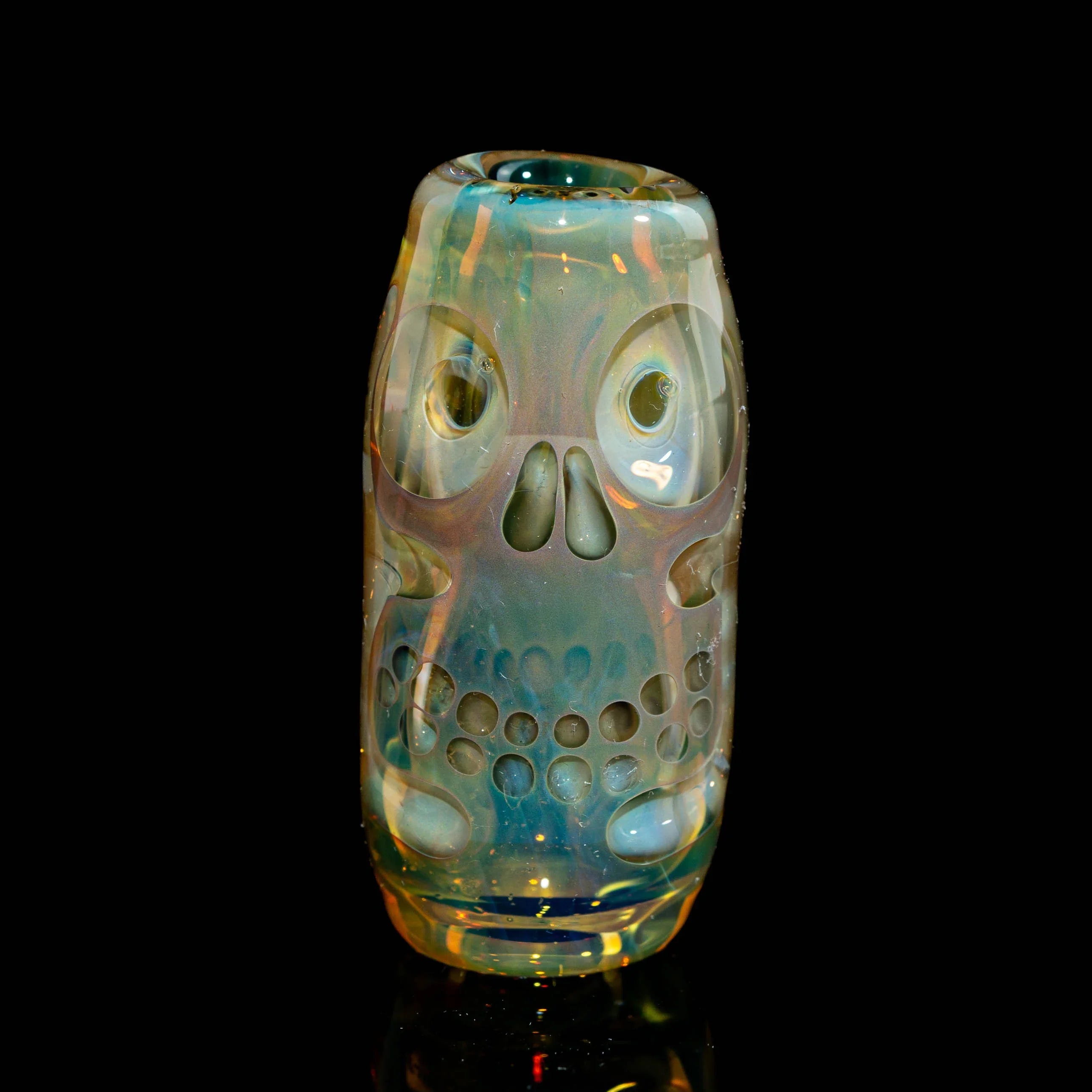 Handblown glass cup with iridescent skull design, artisan glass art under studio lighting