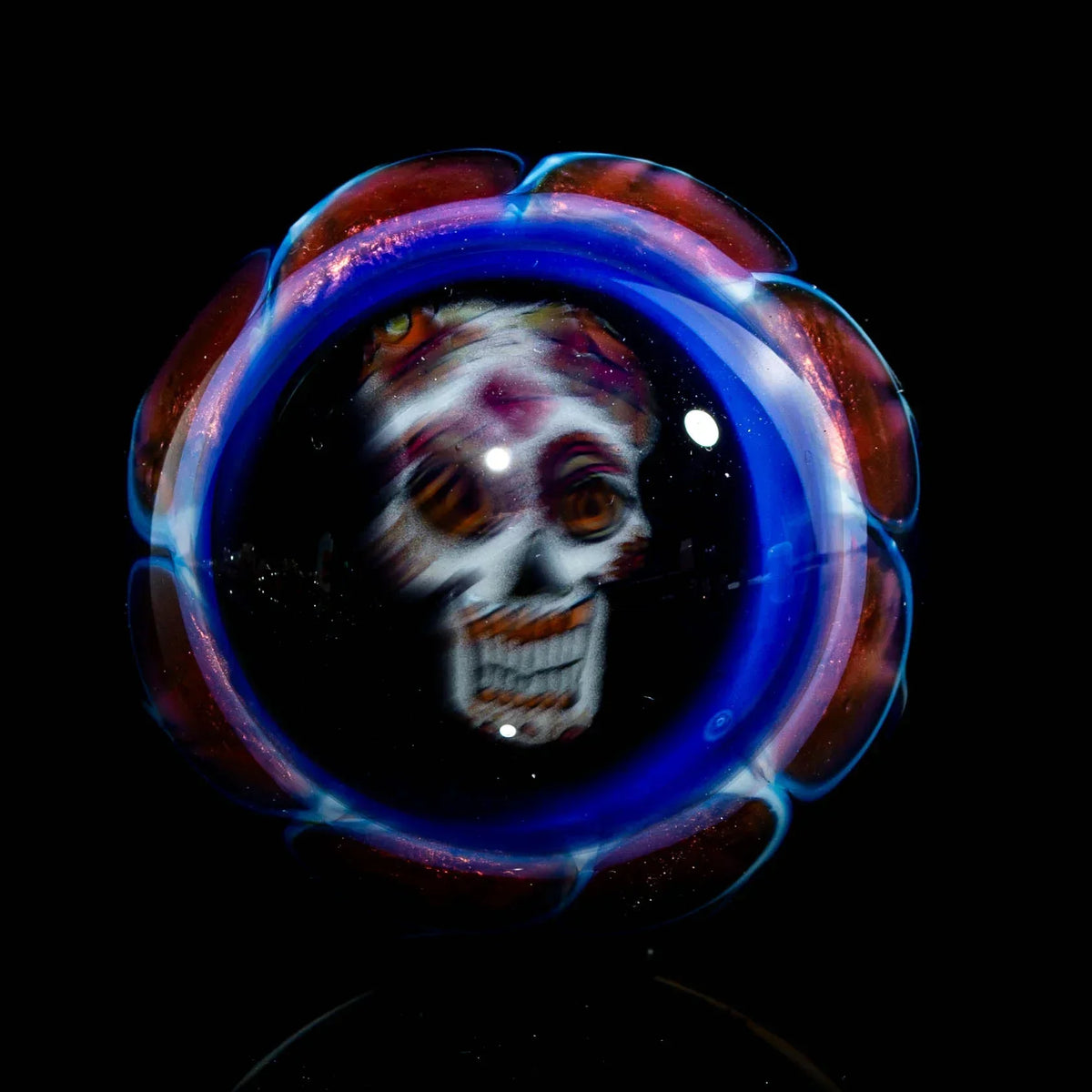 Handcrafted glass marble with intricate skull design and blue-red accents on black background