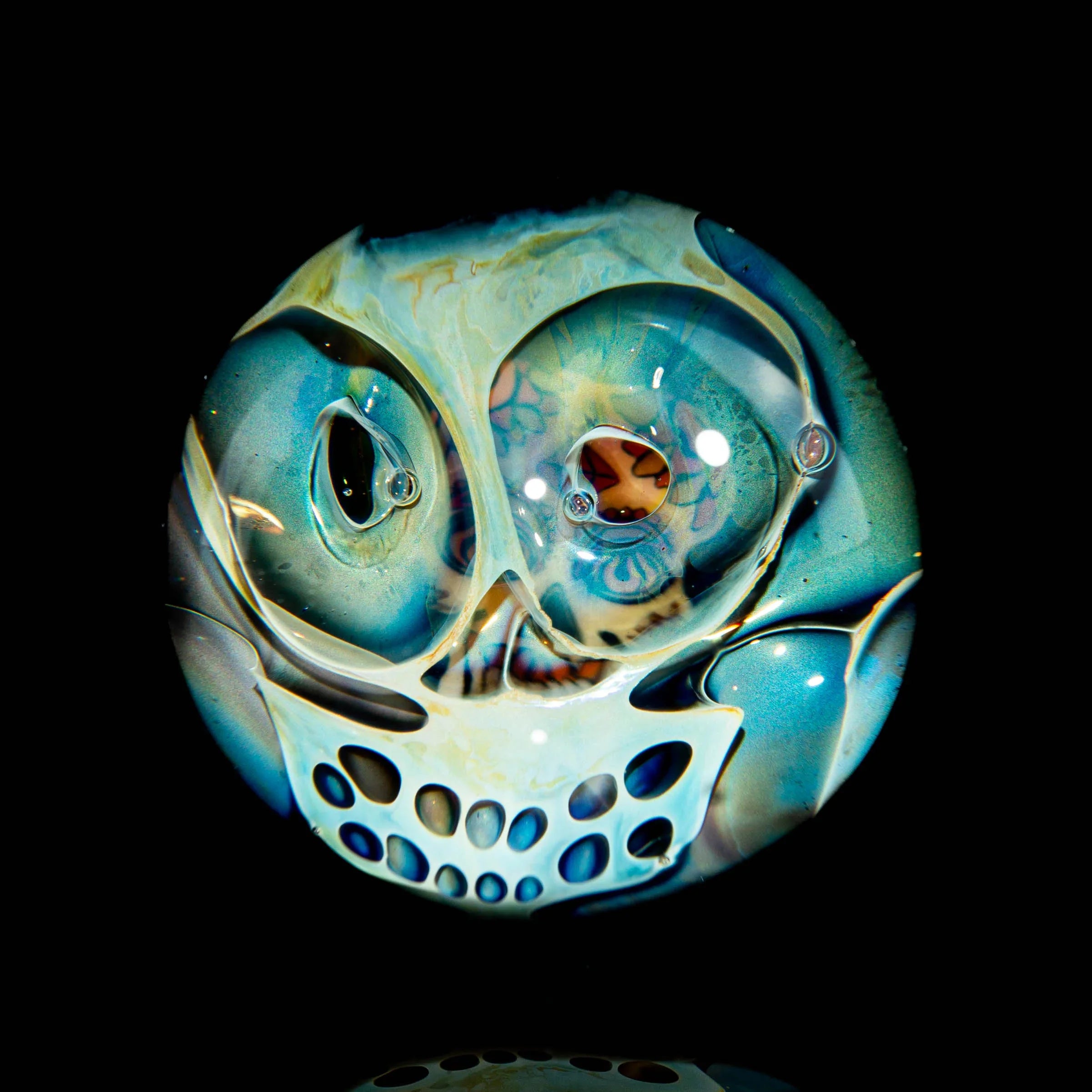 Hand-blown glass marble with intricate skull design and multicolored accents on black background