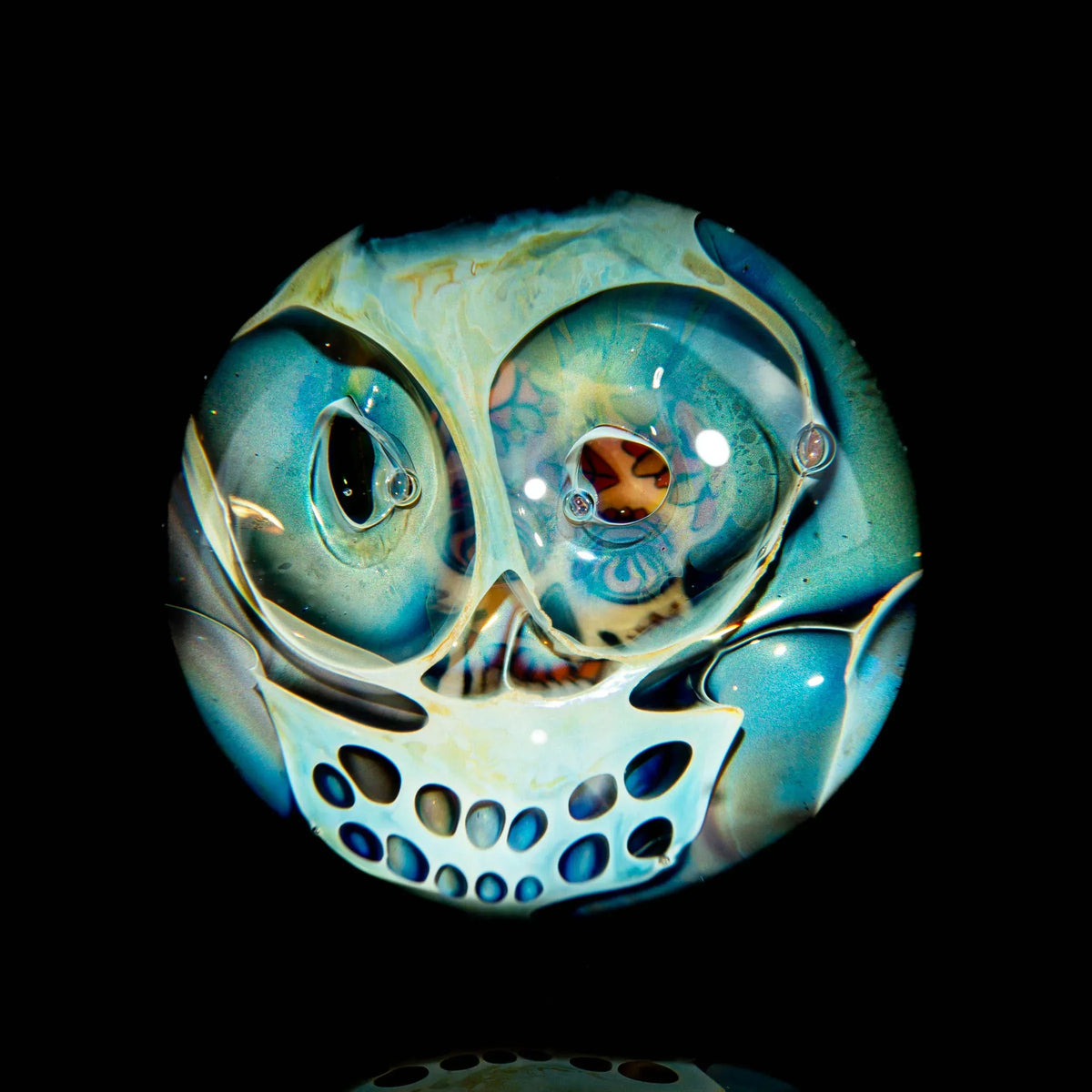 Hand-blown glass marble with intricate skull design and multicolored accents on black background