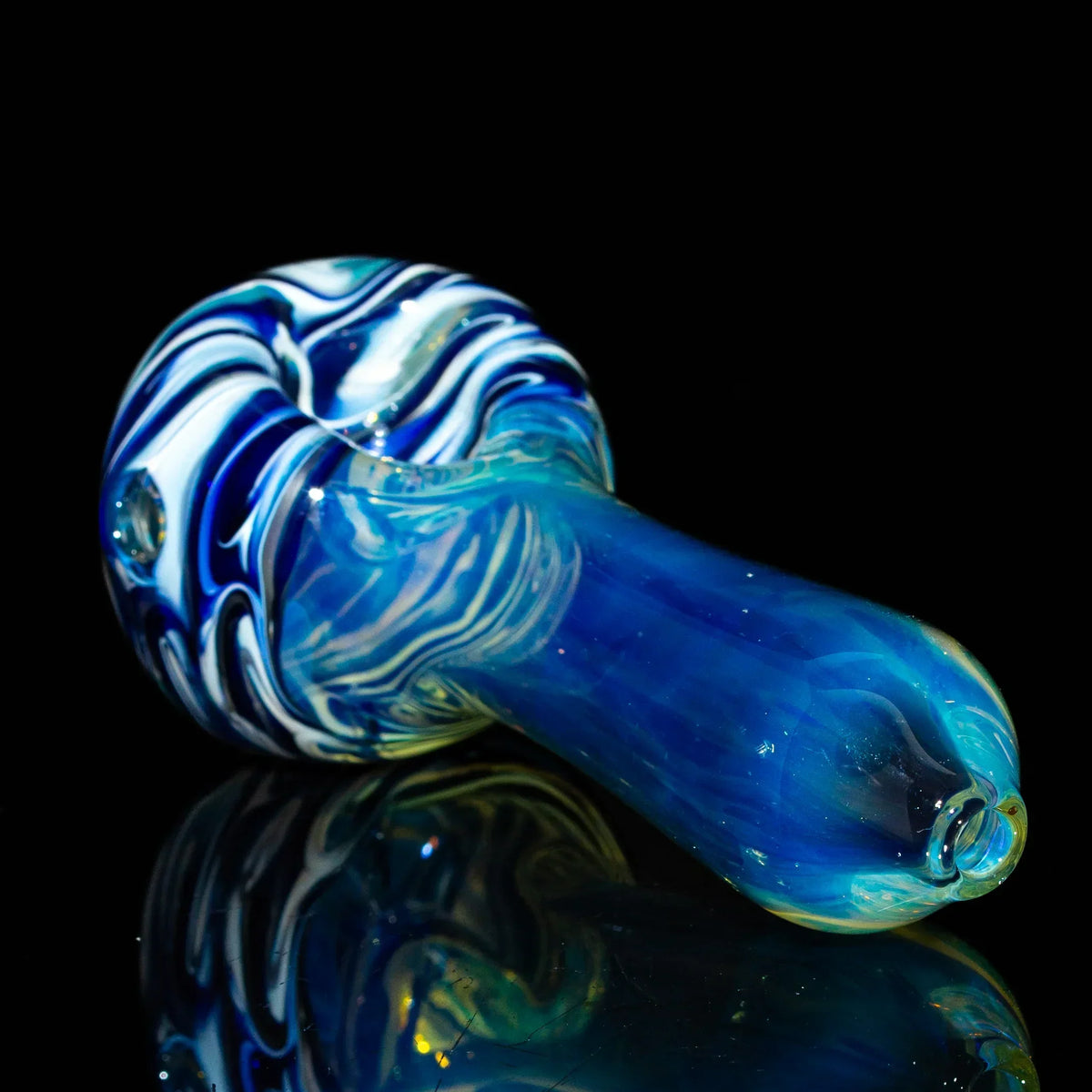Blue and white glass spoon pipe with fumed accents on a black reflective surface