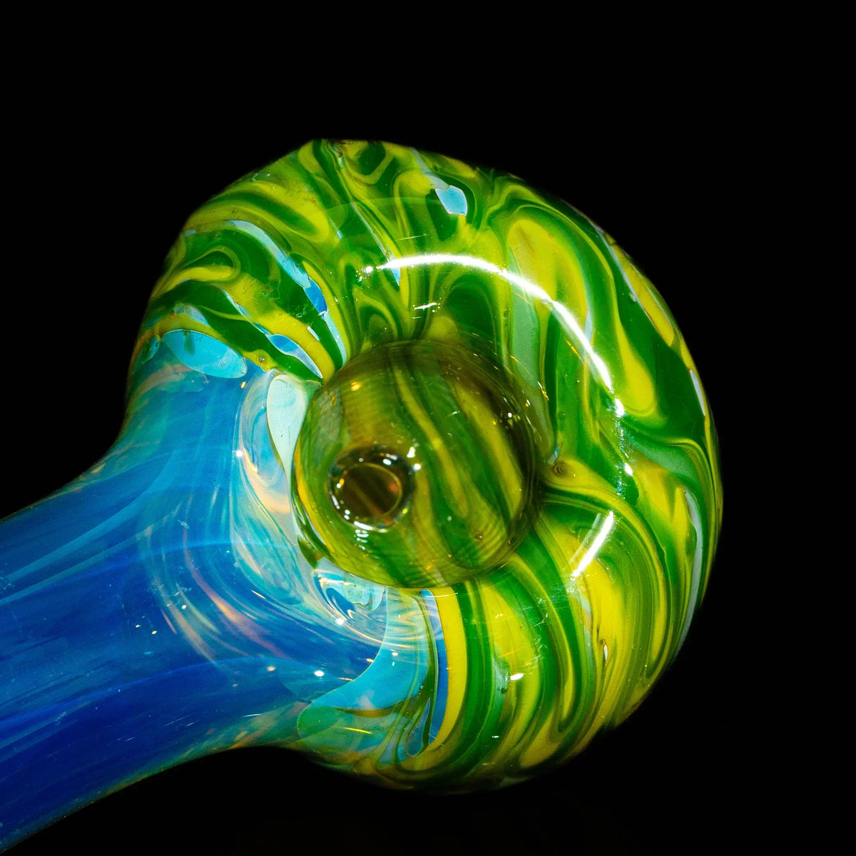 Close-up of green and yellow swirl glass spoon pipe with blue handle on black background.