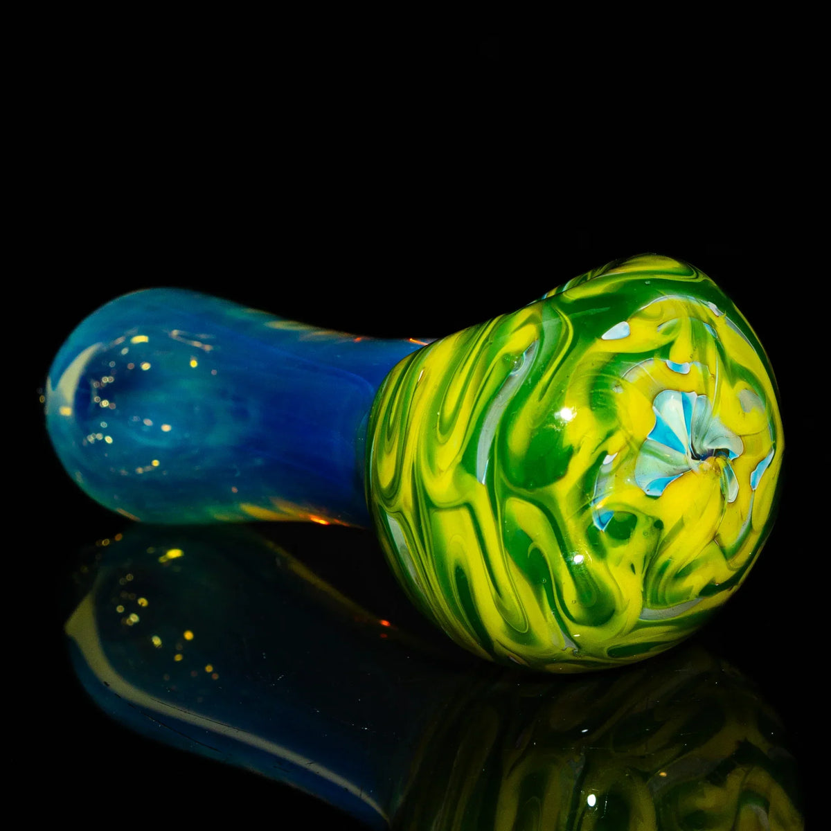 Green and yellow glass hand pipe with blue stem on black background