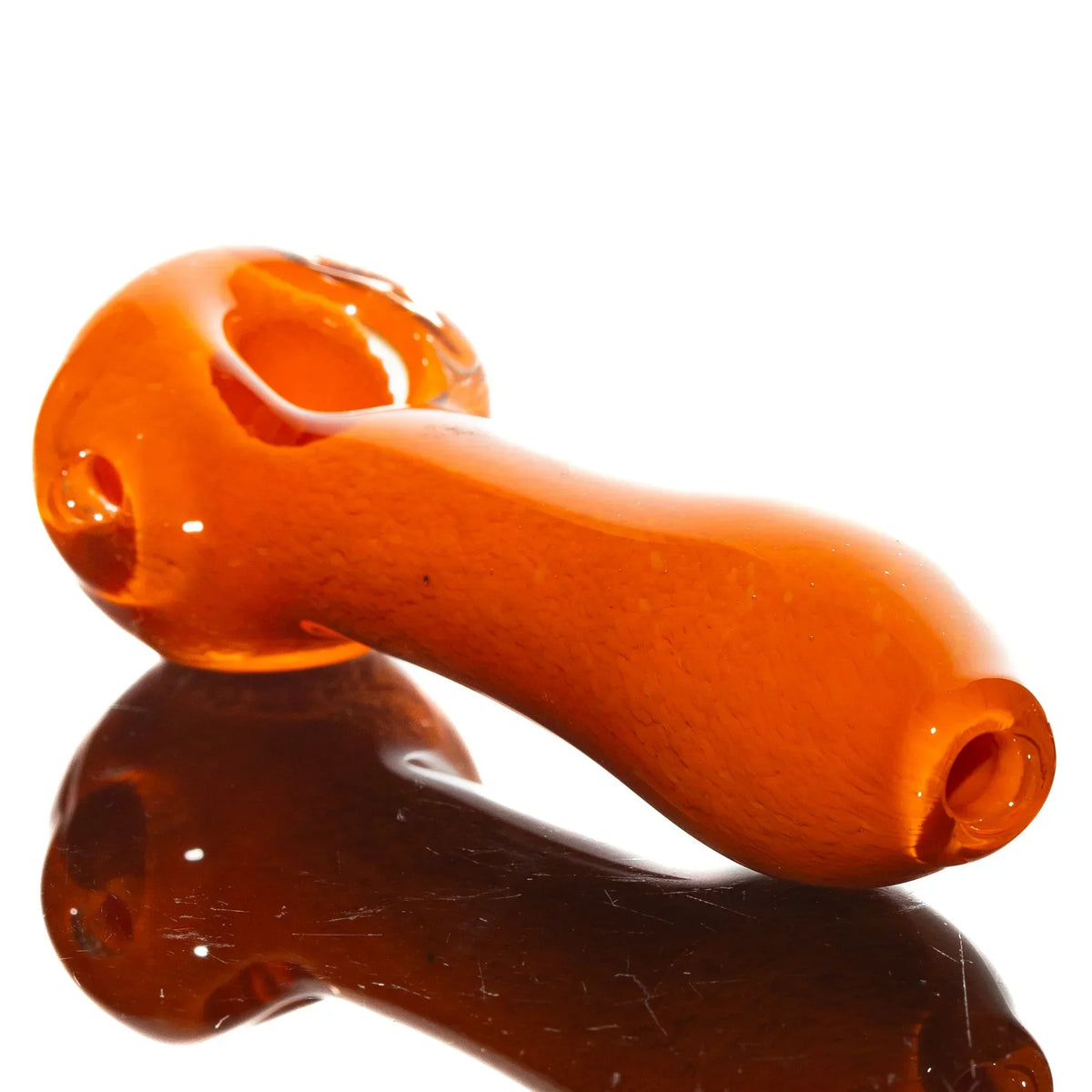 Orange glass hand pipe with frit detail, resting on reflective surface