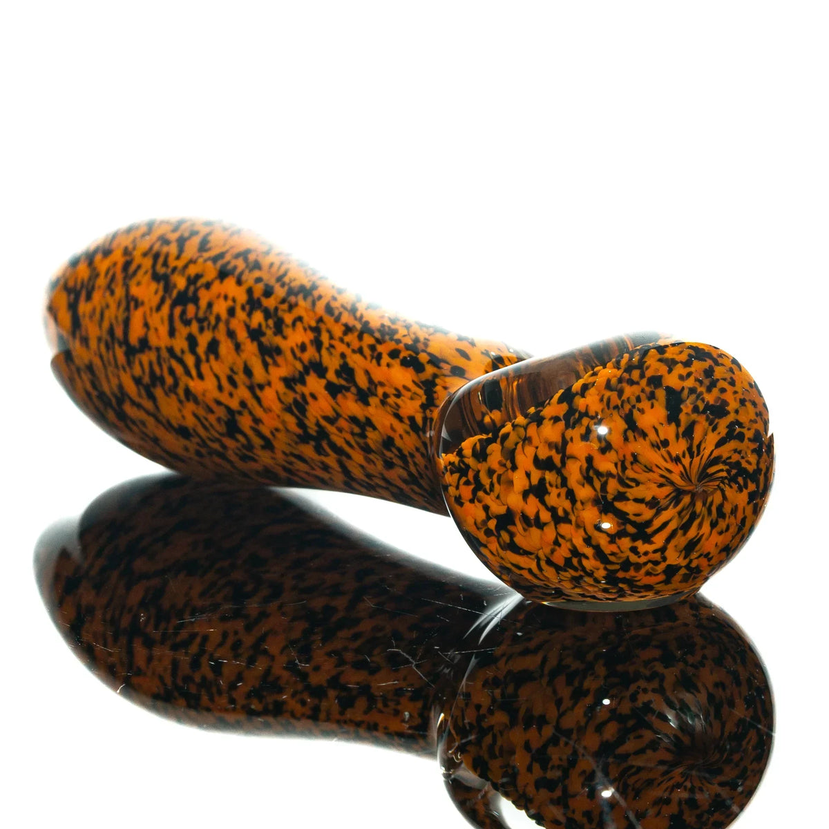 Orange and black frit glass spoon pipe with speckled design on reflective surface