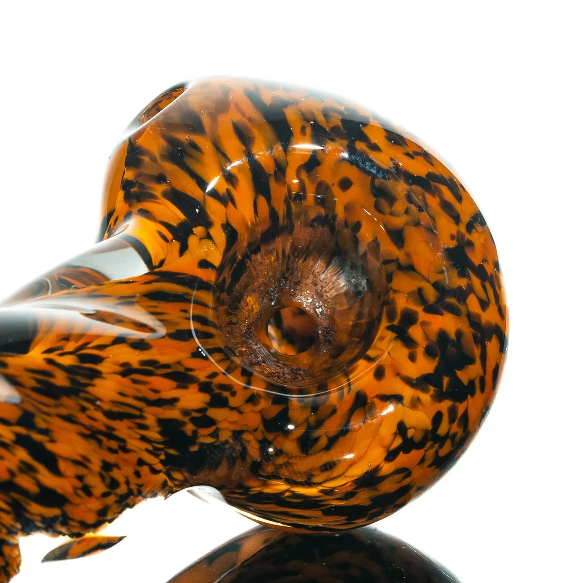 Close-up of orange and black frit glass hand pipe with twist pattern on reflective surface