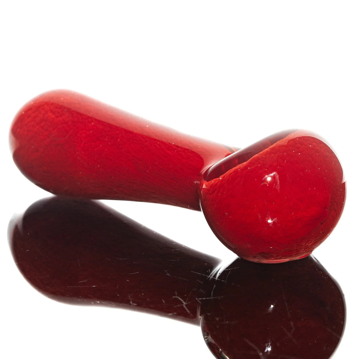 Red glass hand pipe with a spoon shape on a reflective surface