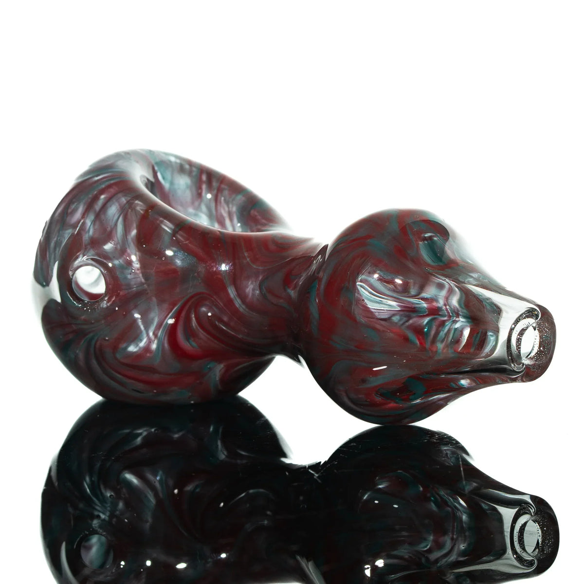 Red and teal glass hand pipe with swirled design, reflected on black surface