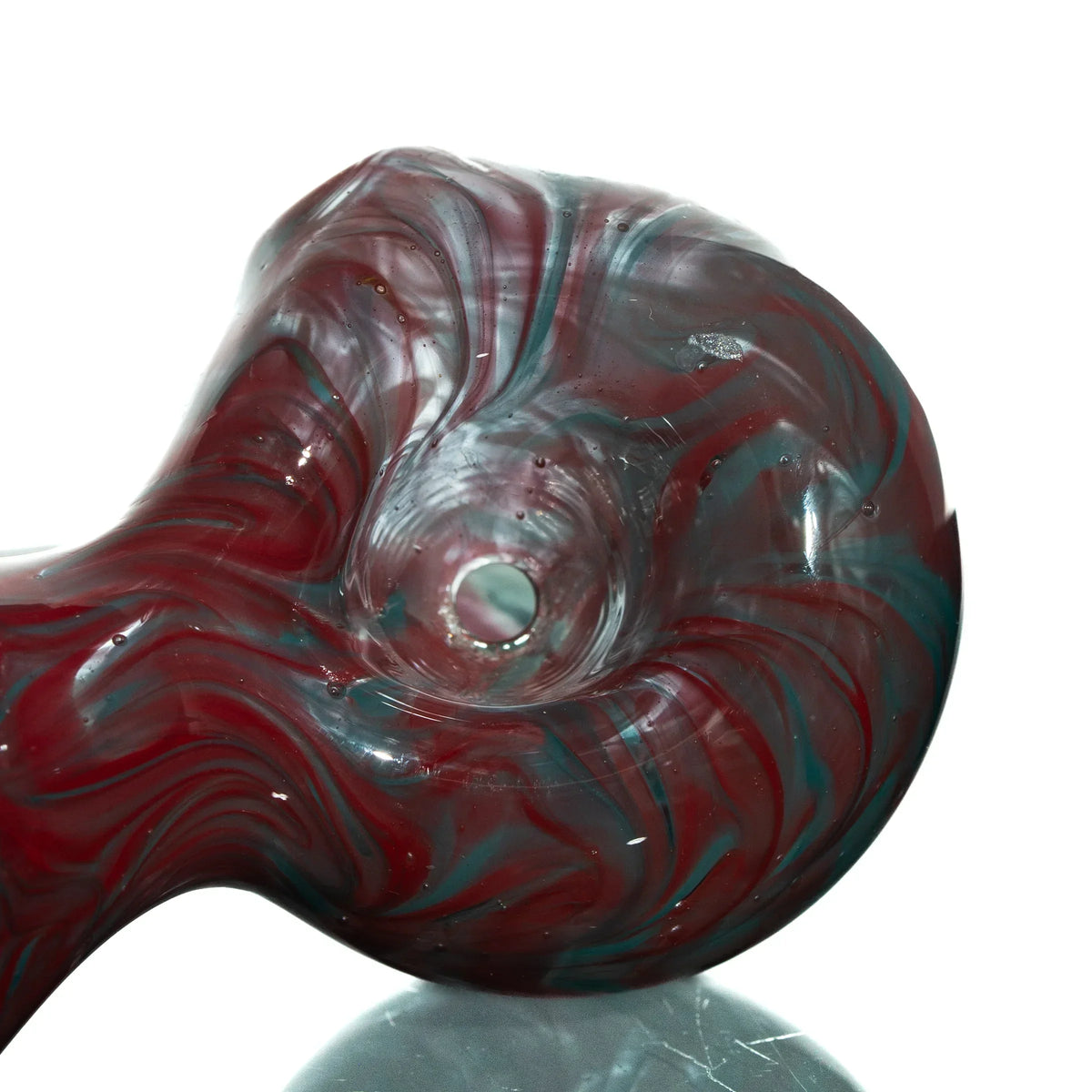 Closeup of red and teal swirl glass spoon pipe on reflective surface