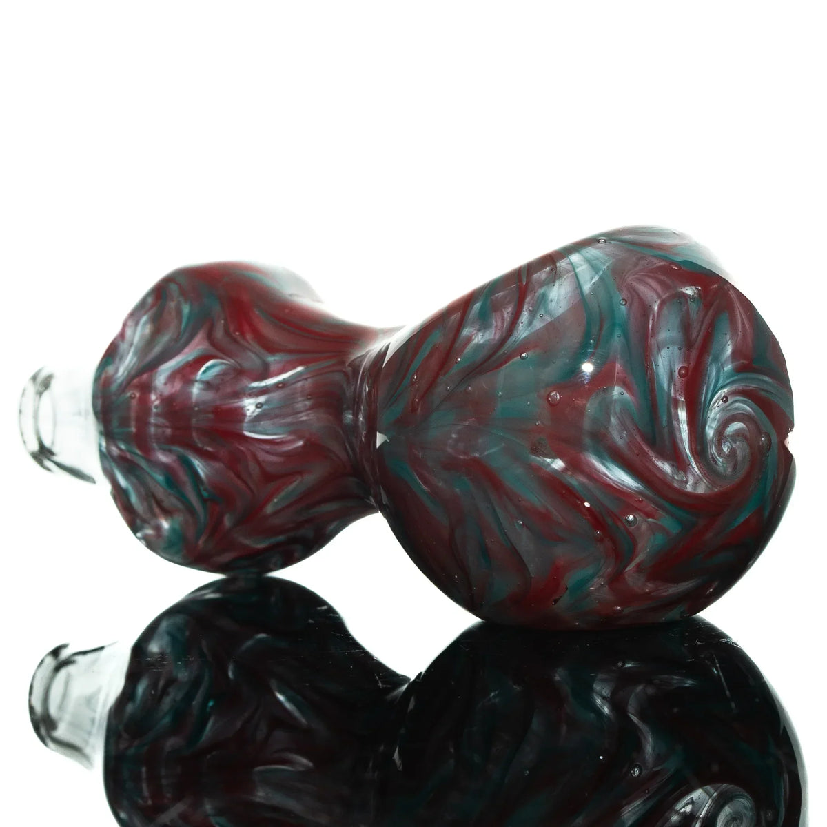 Red and teal swirled glass spoon pipe with hourglass shape on reflective surface