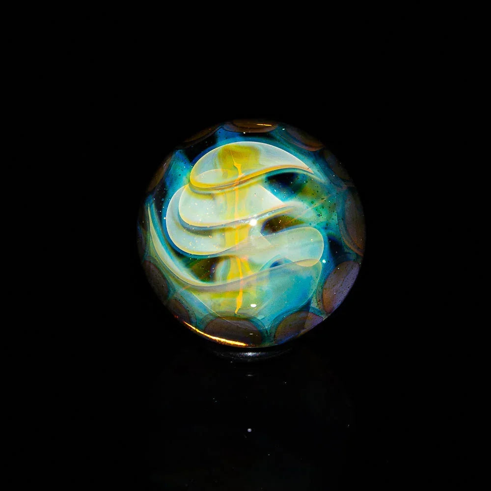 Handcrafted glass marble with swirling blue, yellow, and white patterns on a black background
