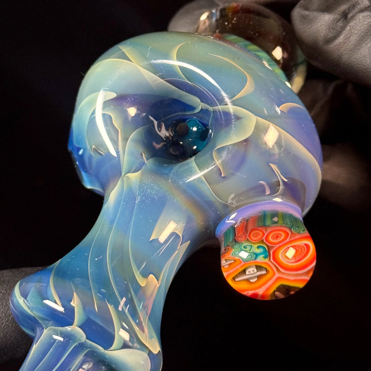 Hand holding a colorful, heady glass pipe with swirling blue and red patterns