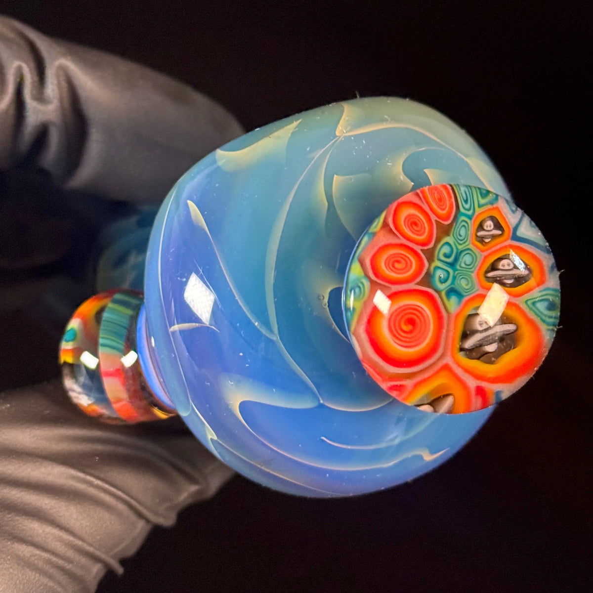 Close-up of a hand holding artisan glass pipe with swirling blue and vibrant red patterns.