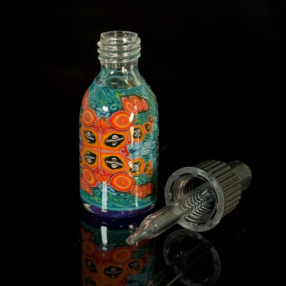 Colorful glass dropper bottle with intricate swirl and face patterns on black background