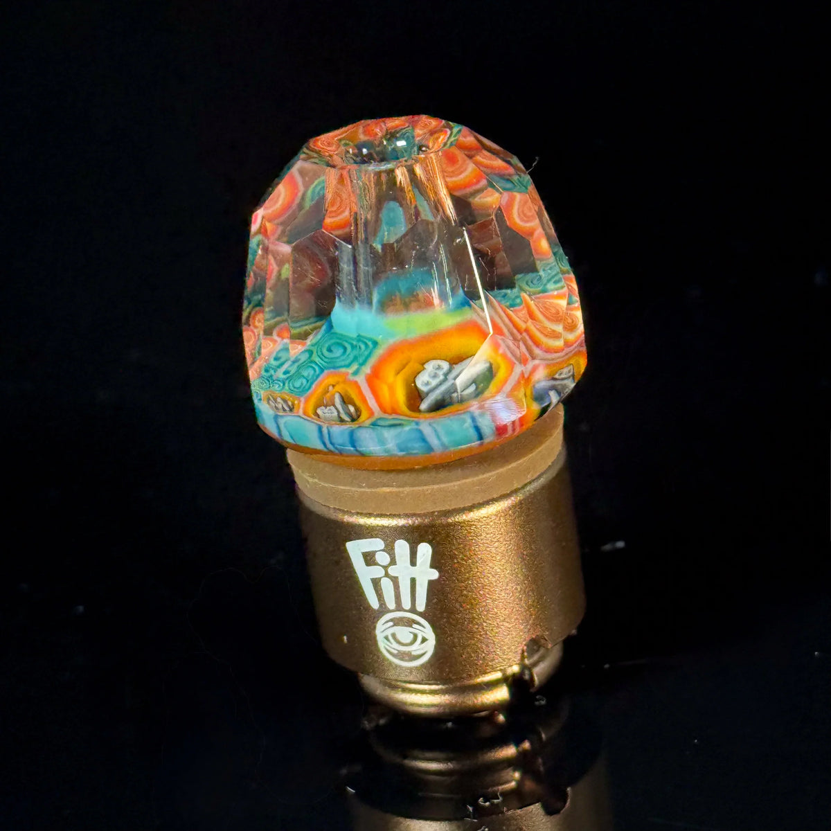 Colorful faceted glass carb cap with intricate patterns on a gold base for vaporizers.