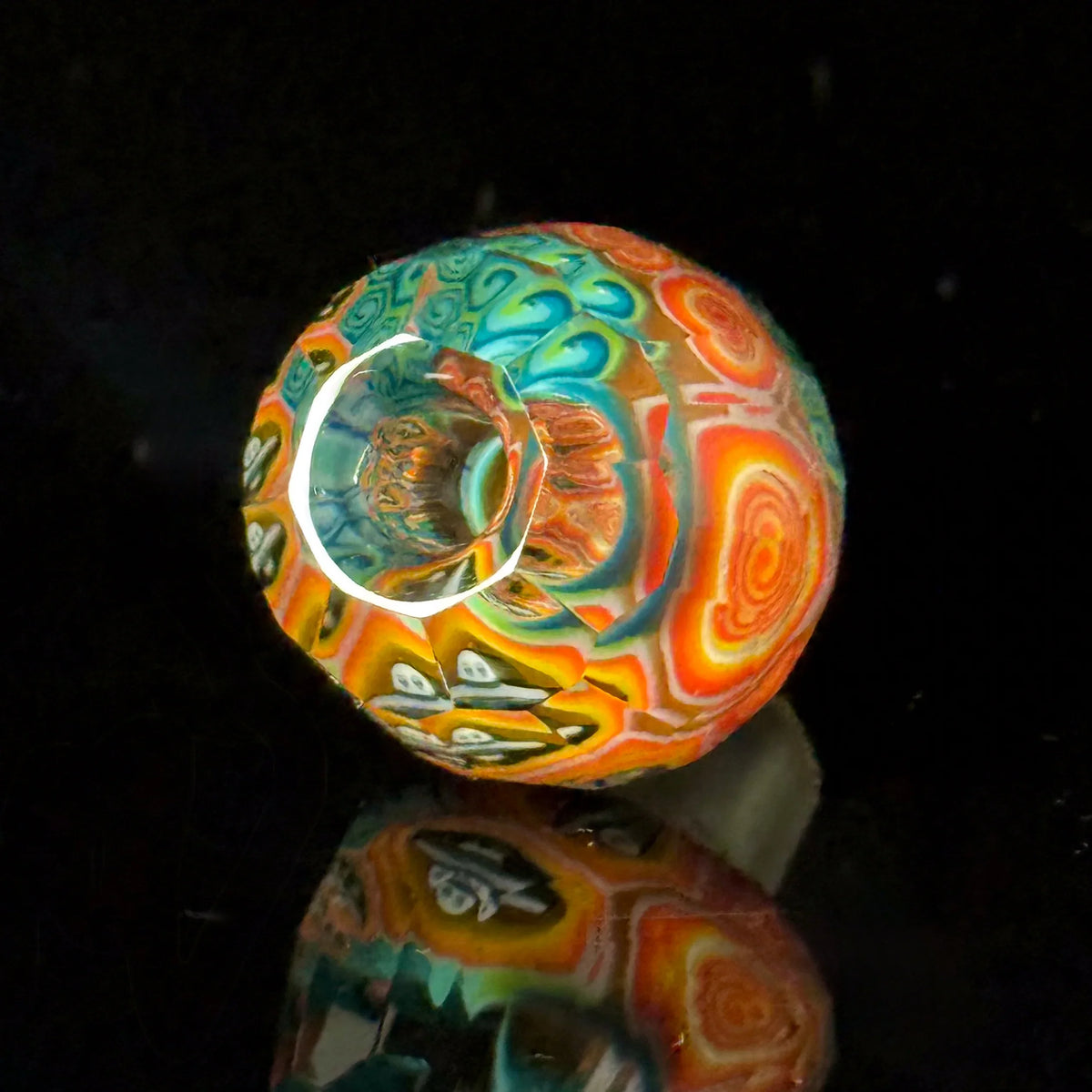 Colorful heady glass pipe with intricate patterns reflecting on a black surface