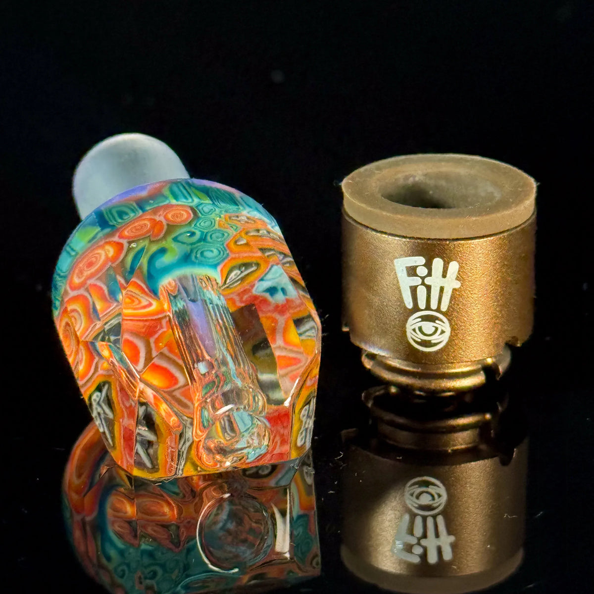 Colorful heady glass attachment and metallic vaporizer accessory with Fitt logo on black surface