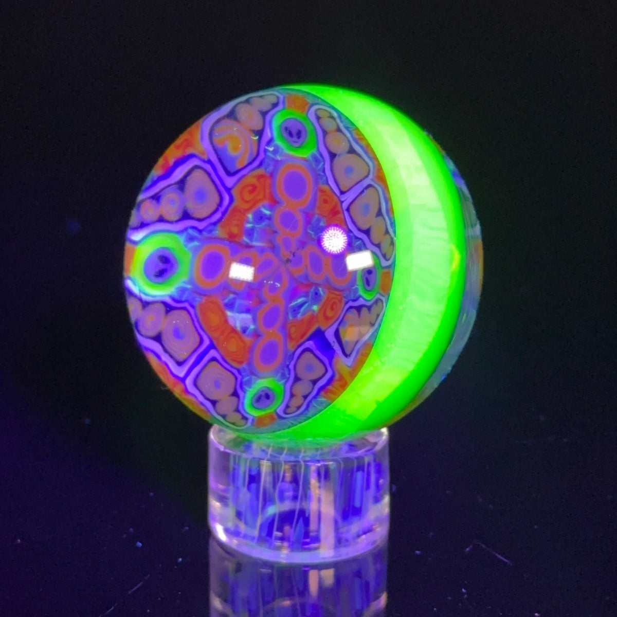 UV reactive glass marble with vibrant neon patterns on a clear stand, glowing under blacklight