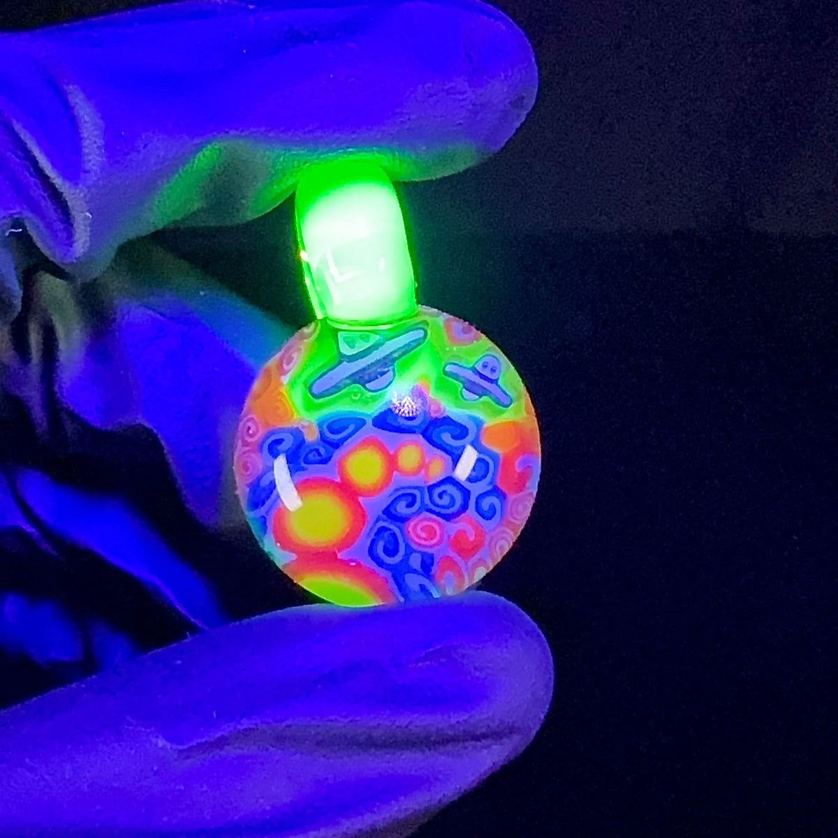 UV reactive glass pendant with colorful swirling patterns and planets, held by gloved hand