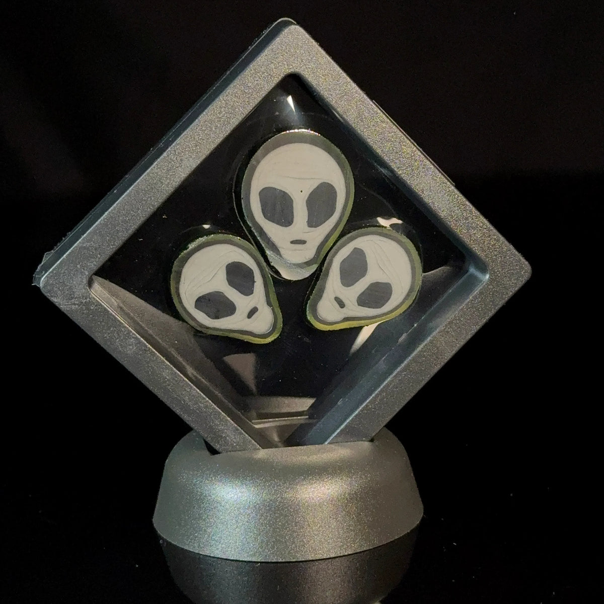 Three glass art pieces with alien faces displayed in a transparent case