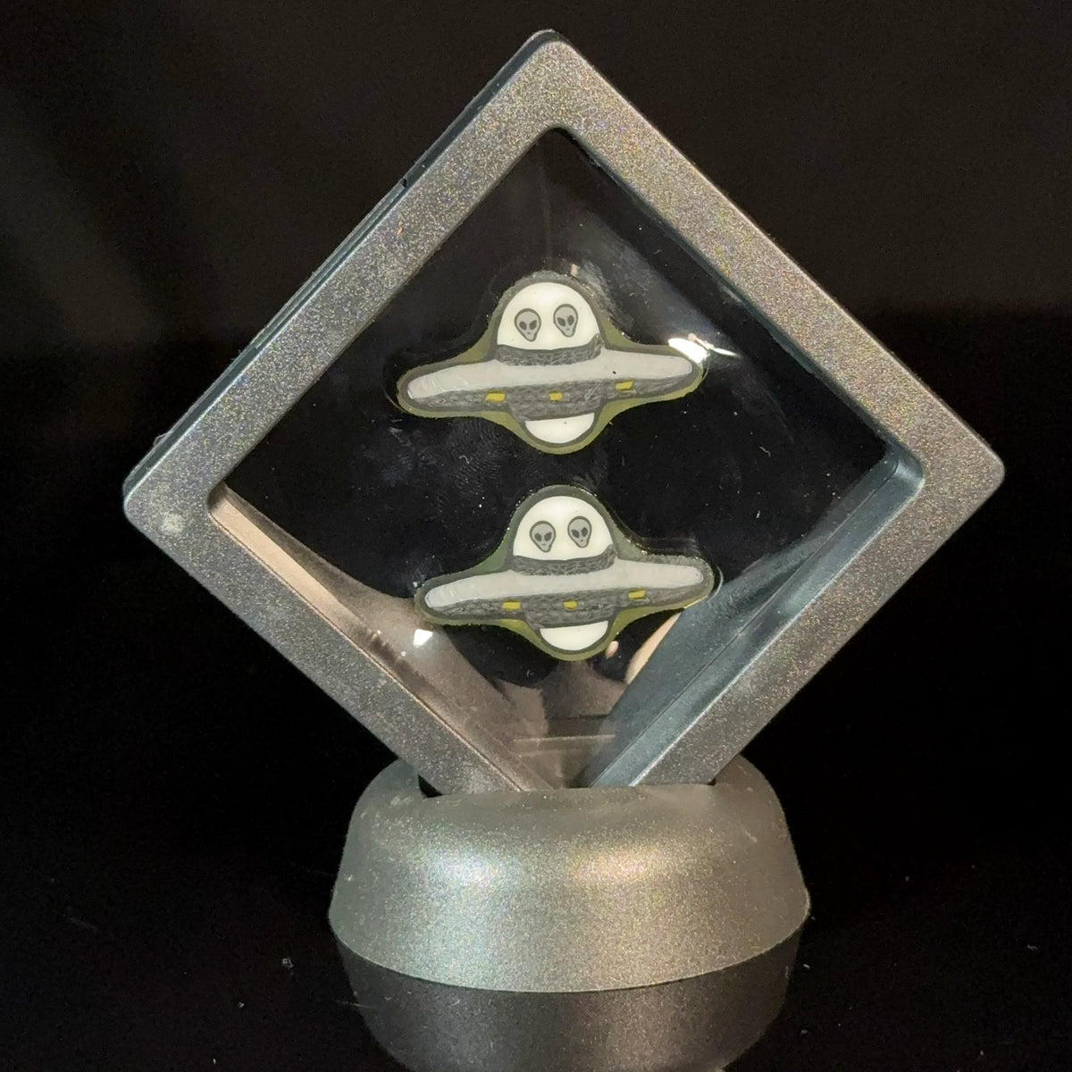 Alien UFO-themed glass art pins displayed in a showcase with black background
