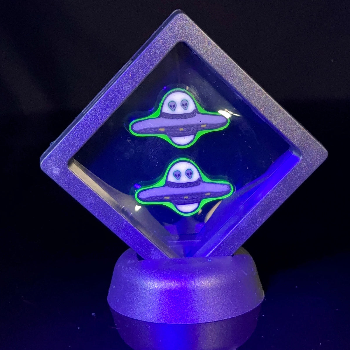 Two UFO-themed glass art pieces with glowing green accents in a clear floating display case