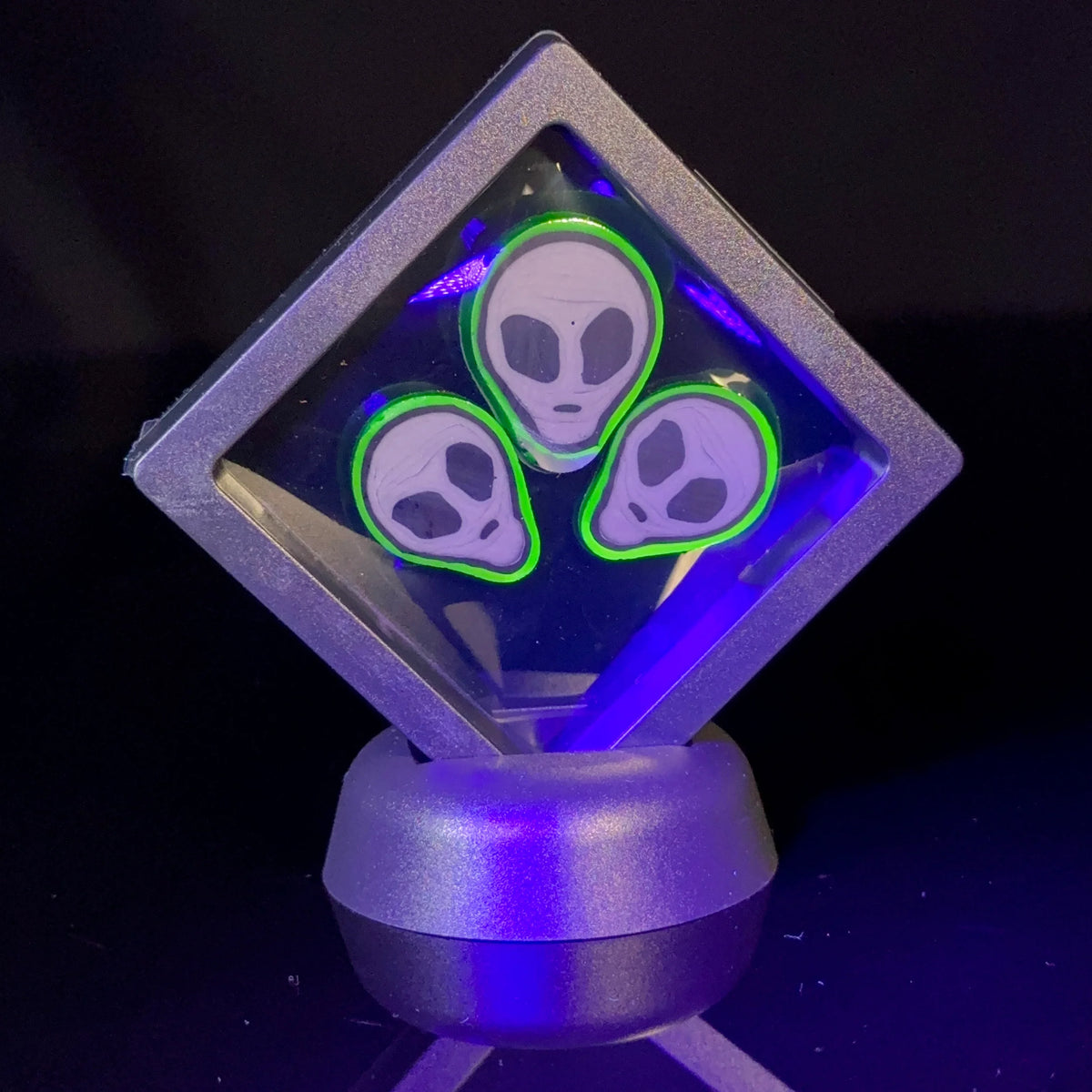 Glowing alien face glass art pin with neon green accents in black display case