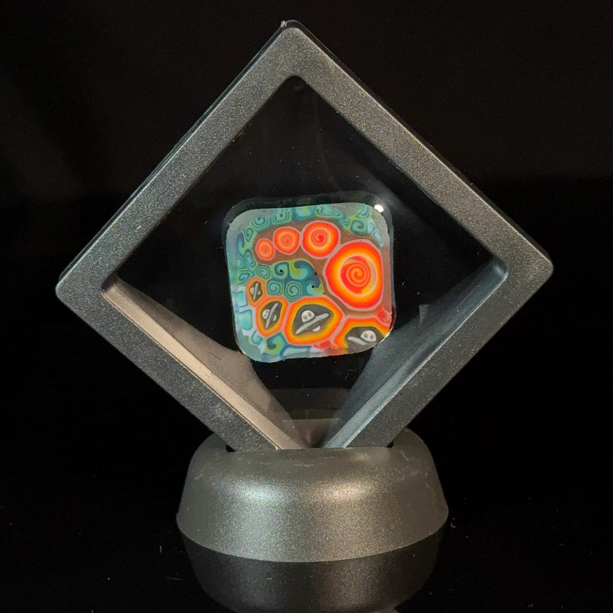 Colorful glass art pendant with spiral and abstract patterns in a display case
