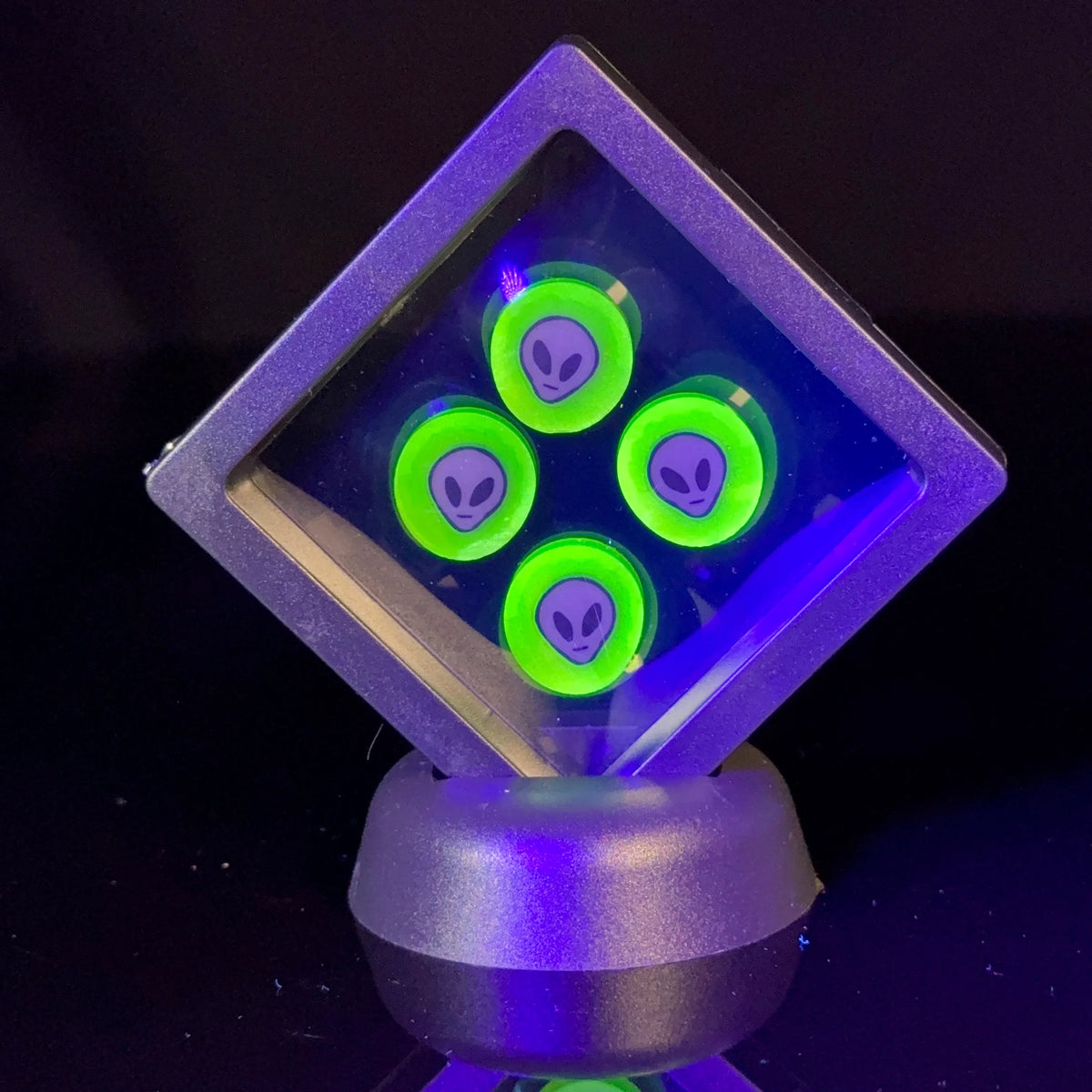 Neon green glass accessories with alien faces displayed in a clear case on a black background