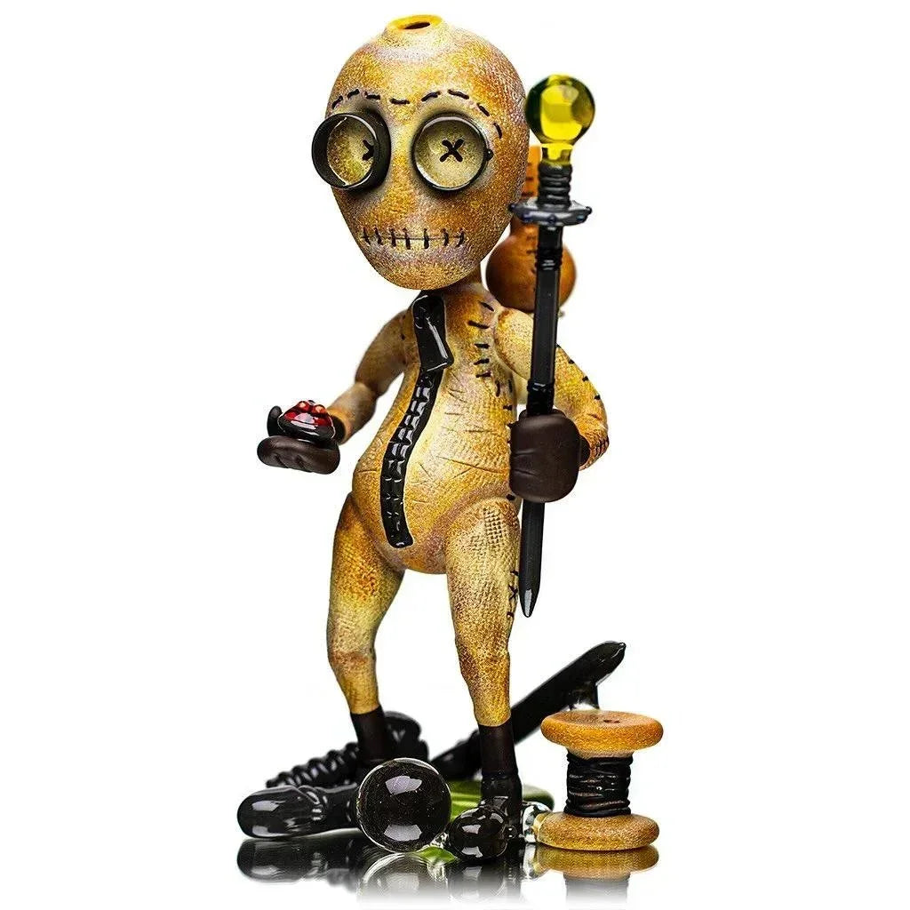 Heady glass art sculpture shaped like a stitched button-eyed figure holding a staff on white background.