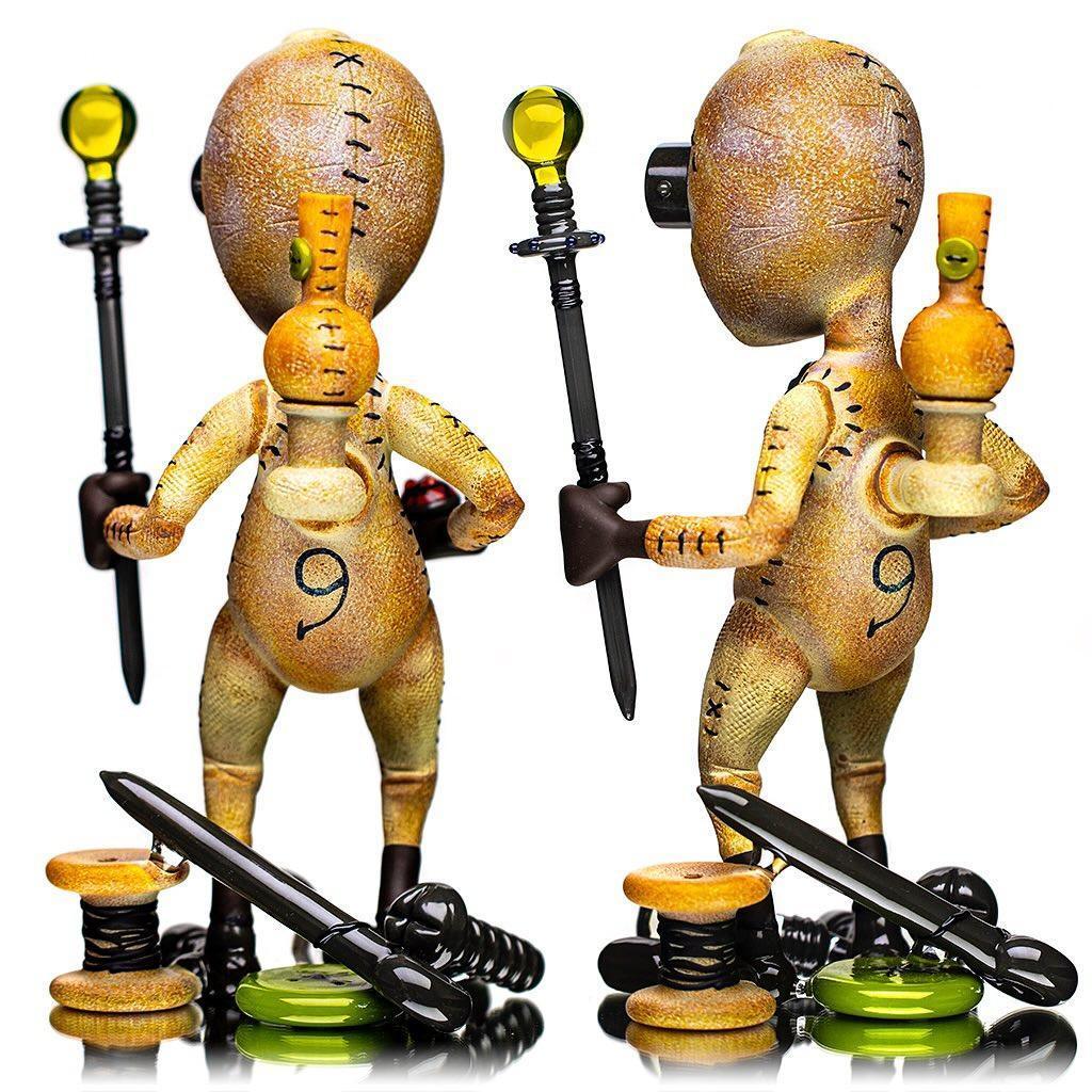 Heady glass art figure with stitched texture, holding staff and bottle, on reflective surface