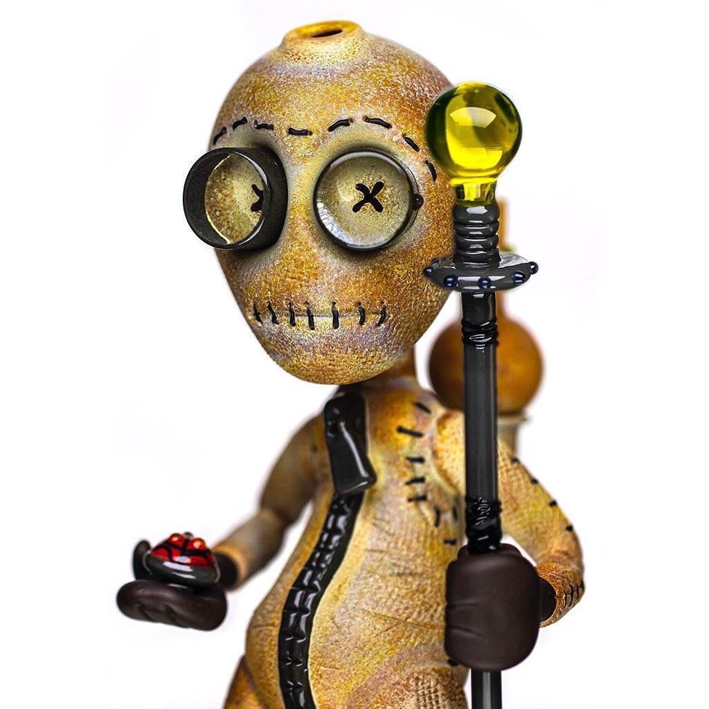 Heady glass art pipe shaped like a stitched doll figure holding a staff and button accessory.