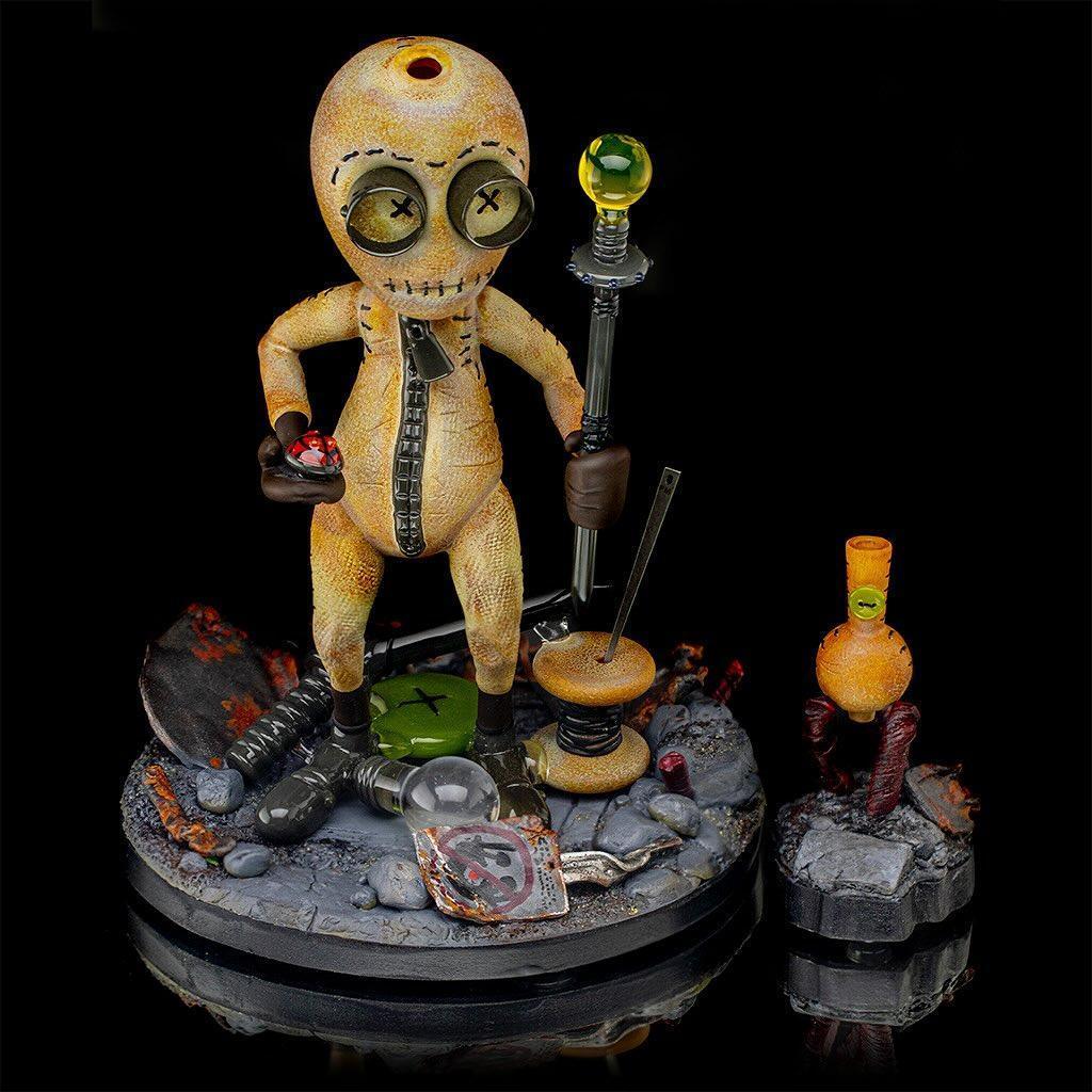 Heady glass art figure with stitched design, button eyes, and accessories on a decorative base