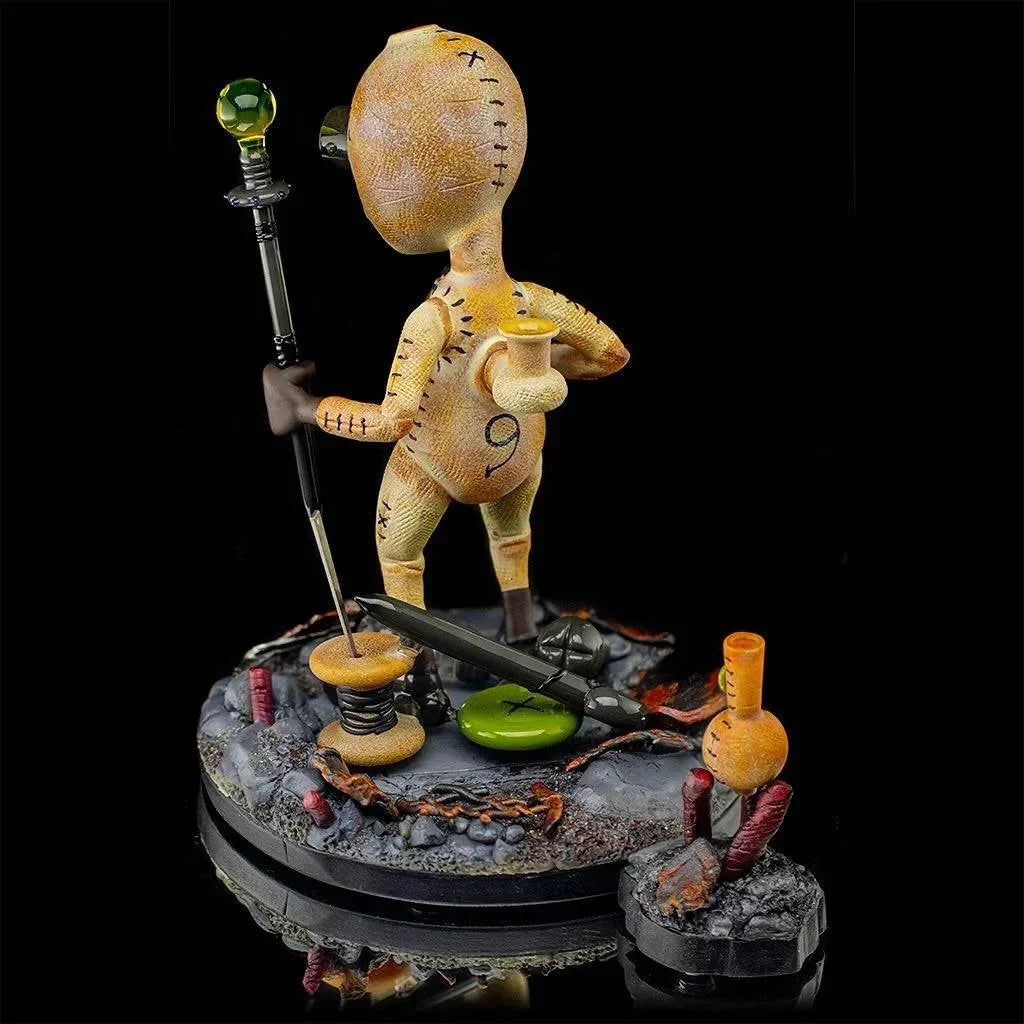 Heady glass art sculpture of a stitched humanoid figure holding a staff and candle on textured base
