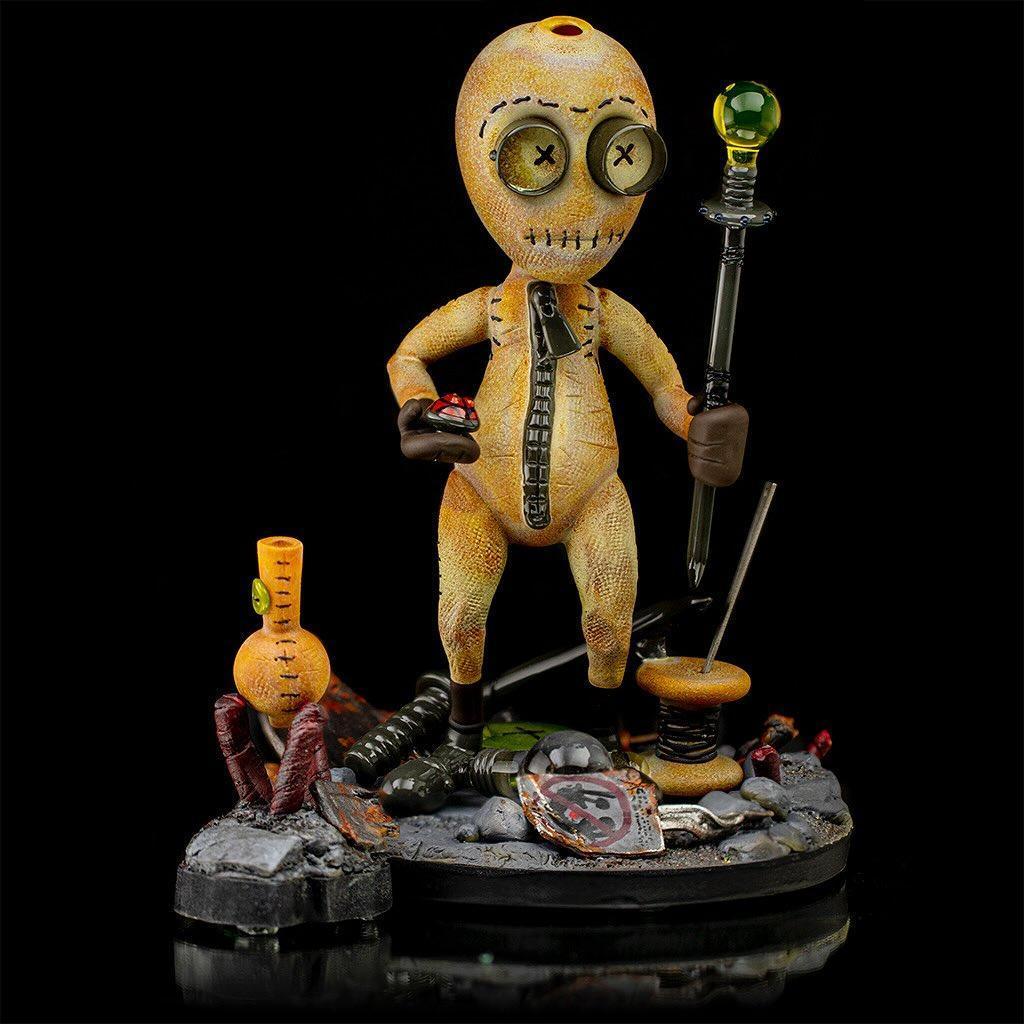 Handcrafted glass art figure resembling a stitched doll, holding a staff and button on a detailed base.