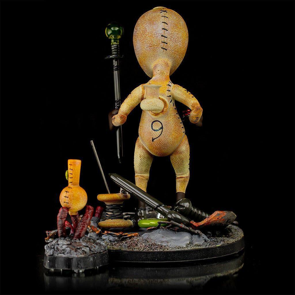 Handcrafted glass art figure with stitched details and accessories on a textured display base.