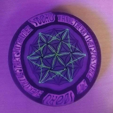 Glass ashtray with geometric glow-in-the-dark design under purple light